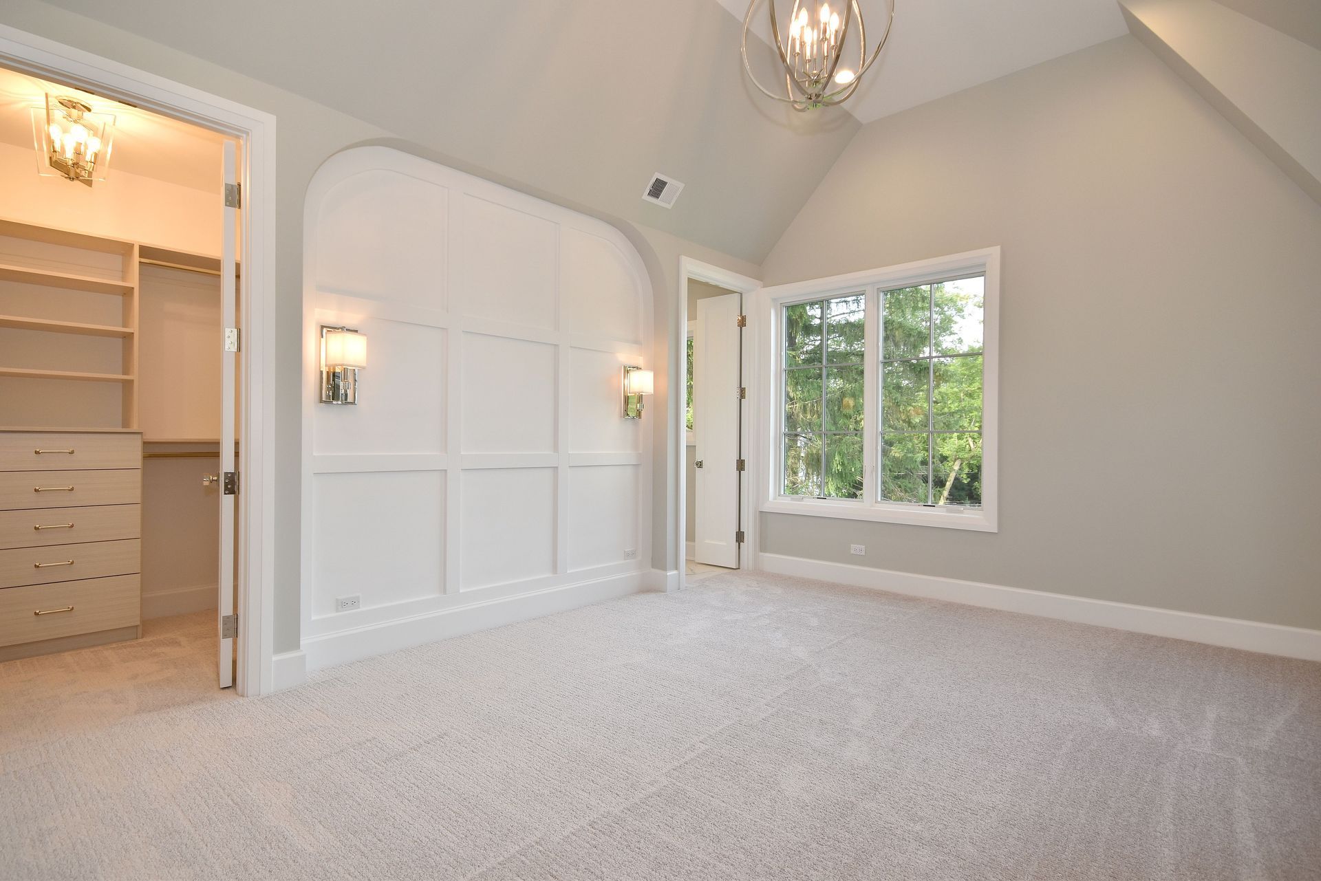 Bright empty bedroom with beige carpet, white walls, double closet doors, and a window overlooking trees
