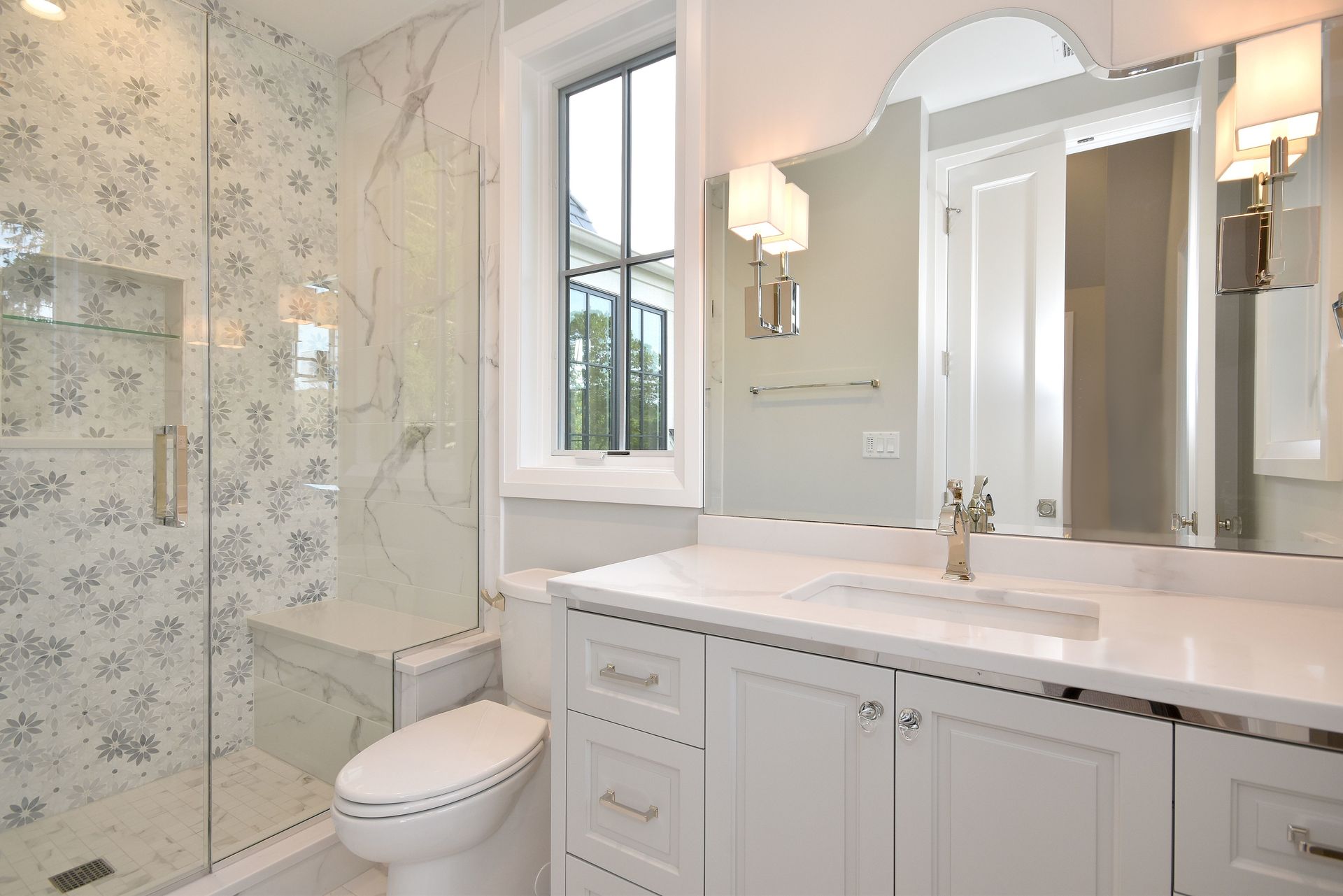 Bright bathroom with floral tile, white vanity, mirror, window, and toilet.