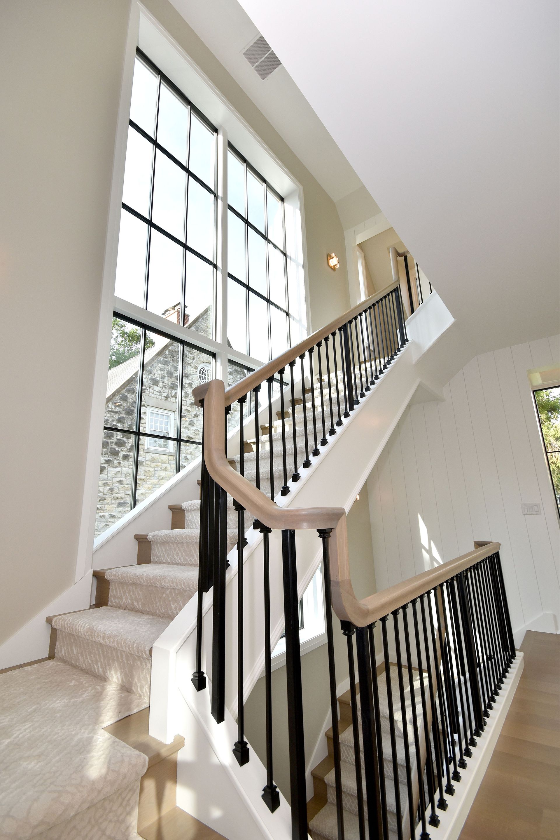 Bright stairwell with beige carpeted stairs, black railings, and large windows letting in natural light