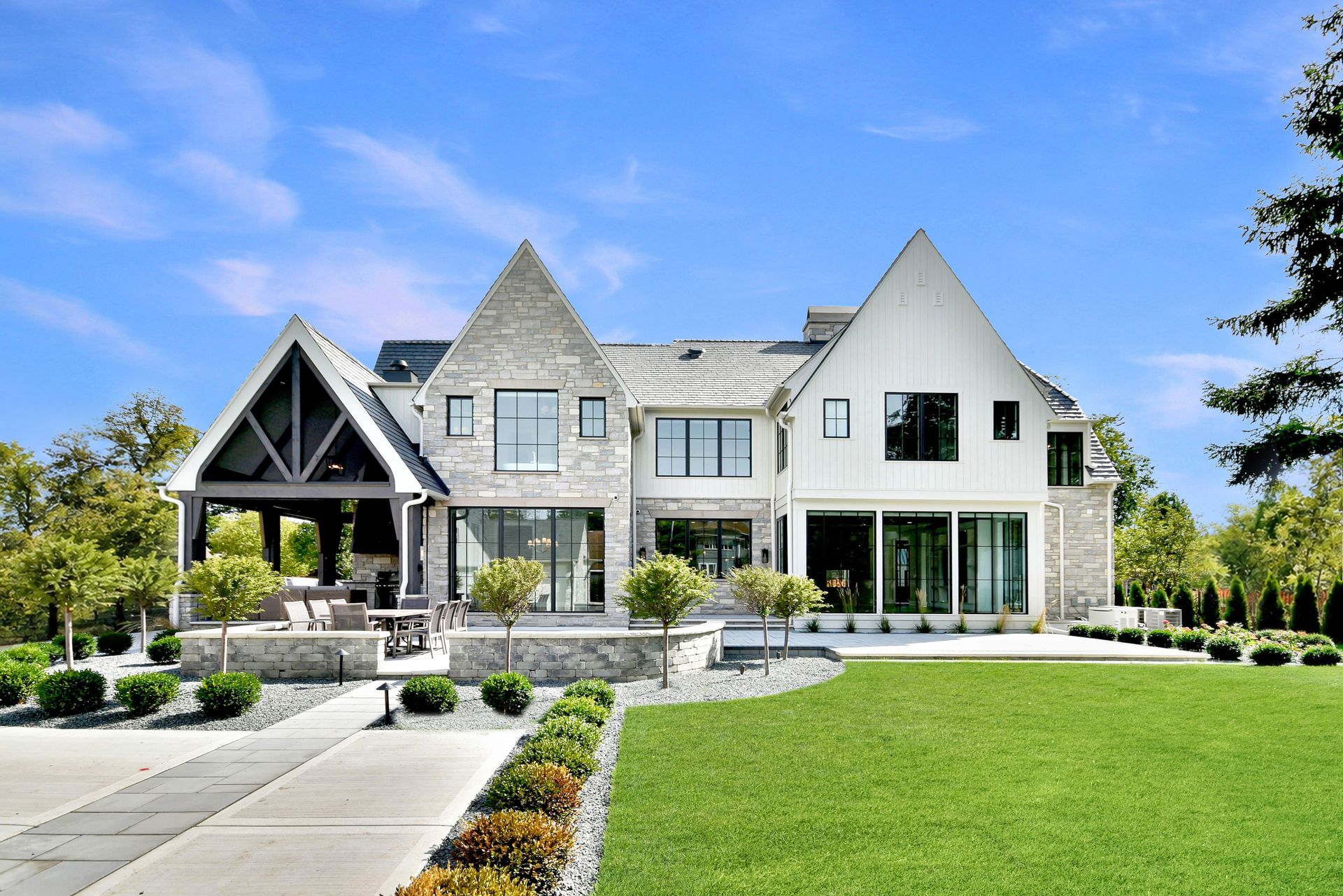 Modern stone house with steep roofs, front lawn, and landscaped walkway under a blue sky