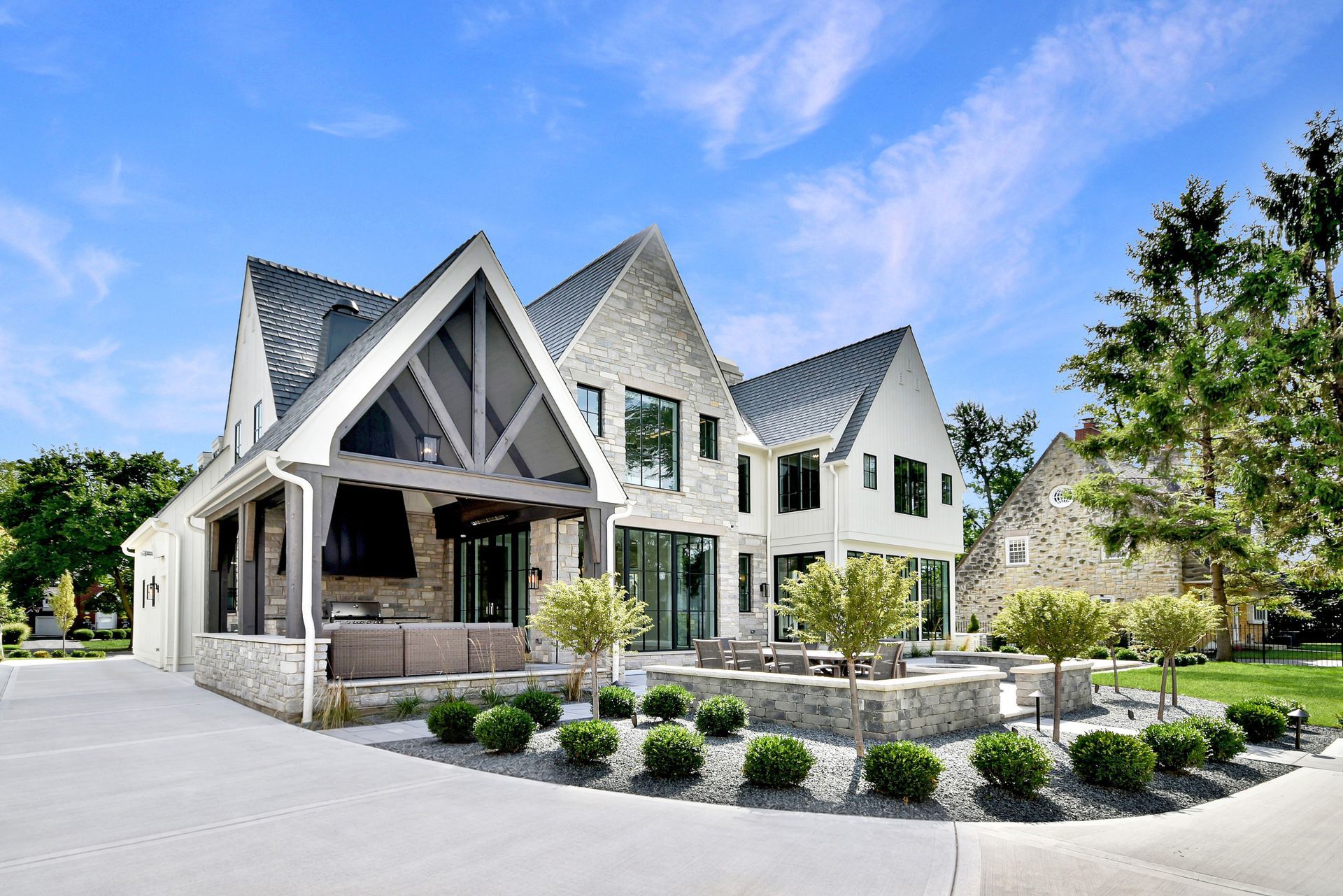 Modern white house with steep gables, stone accents, and a landscaped front yard under a blue sky