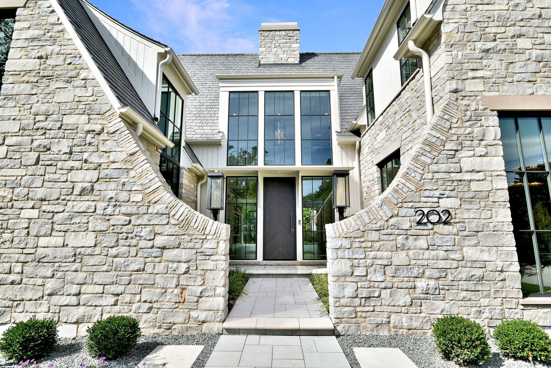 Stone modern house entrance with large windows and a path between two stone walls