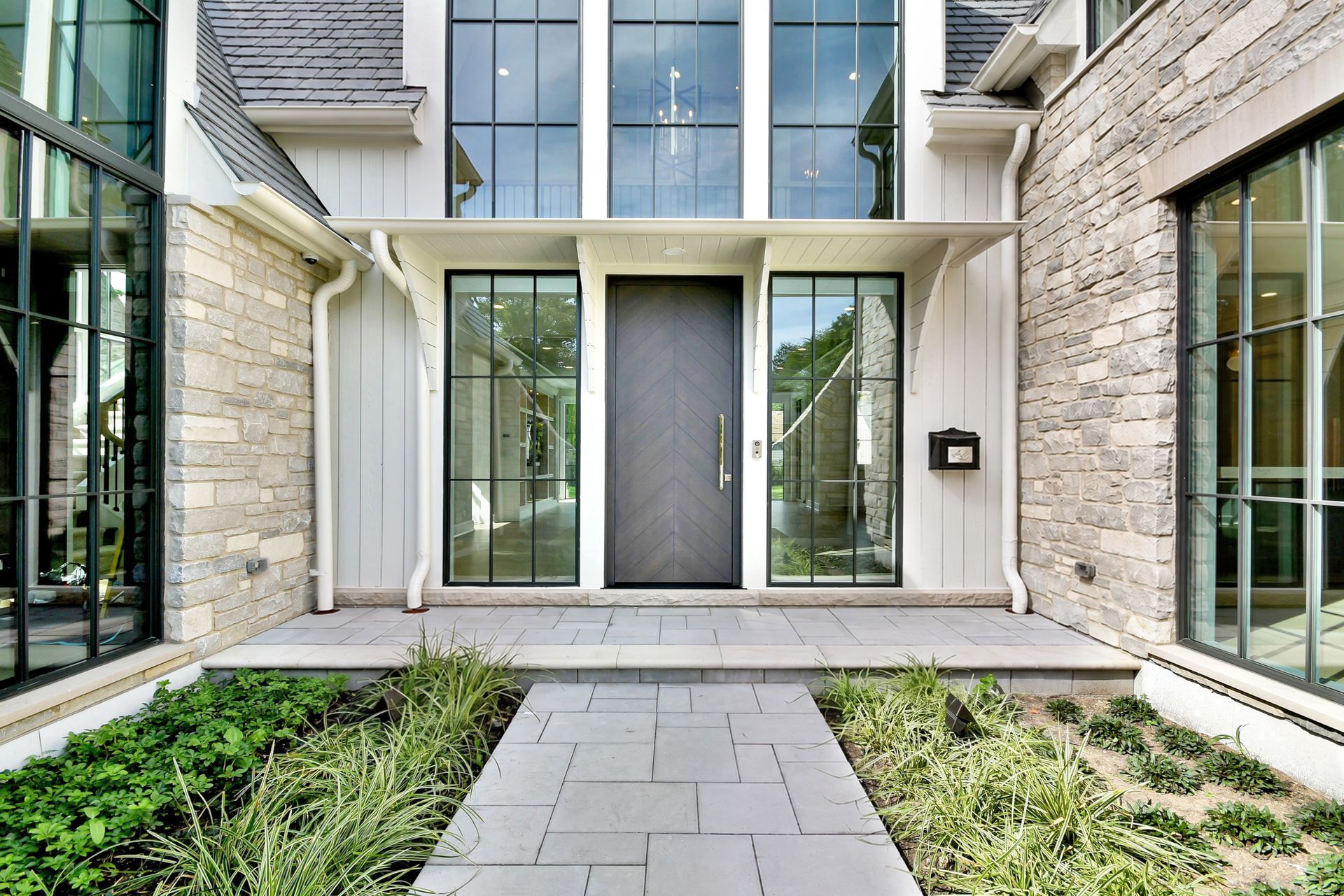 Modern townhouse entrance with glass doors, stone facade, and a landscaped walkway leading to the front steps