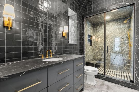 Modern bathroom with black tile, gray vanity, and glass shower door