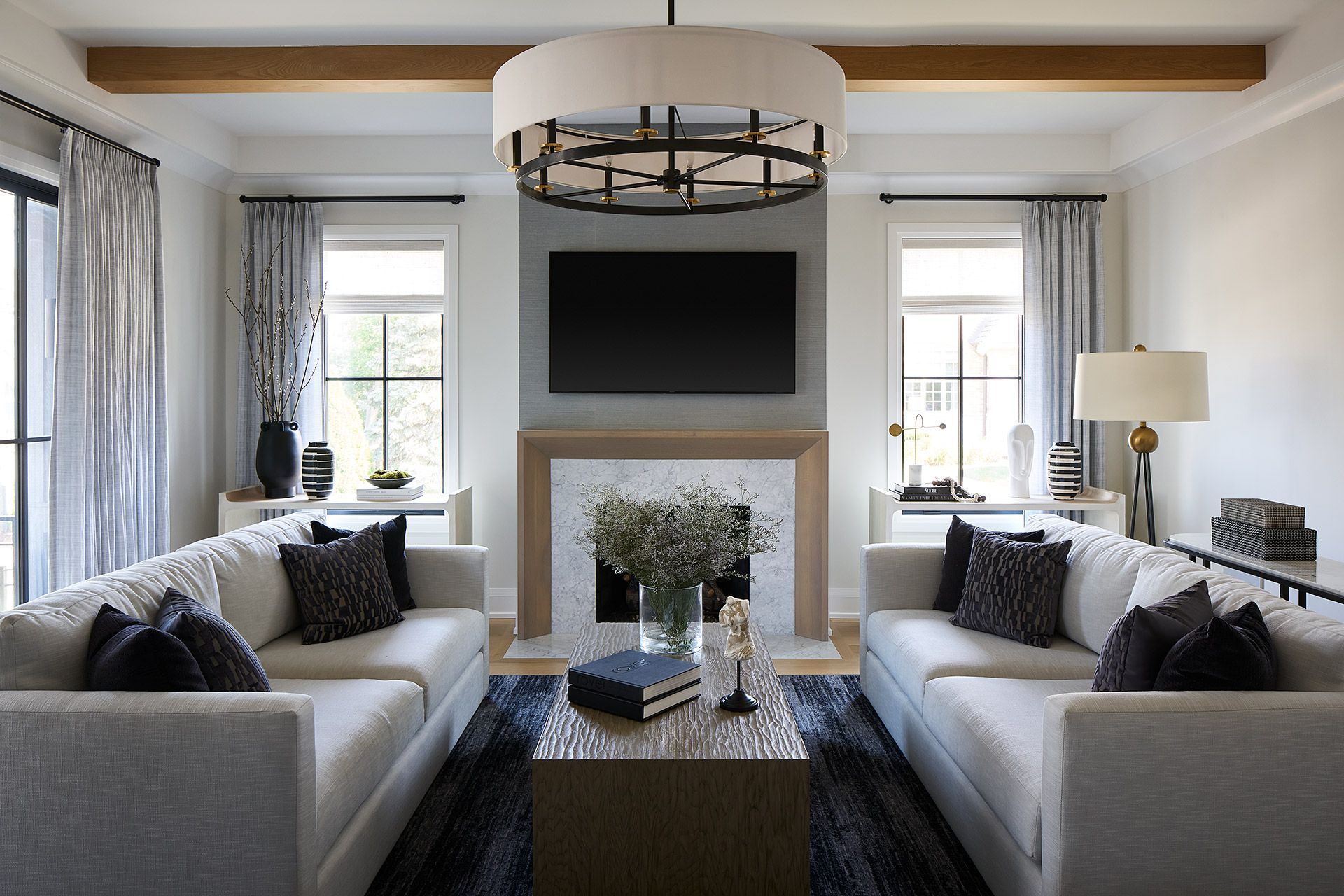 Elegant living room with twin sofas, a fireplace TV, and neutral decor beneath a modern chandelier