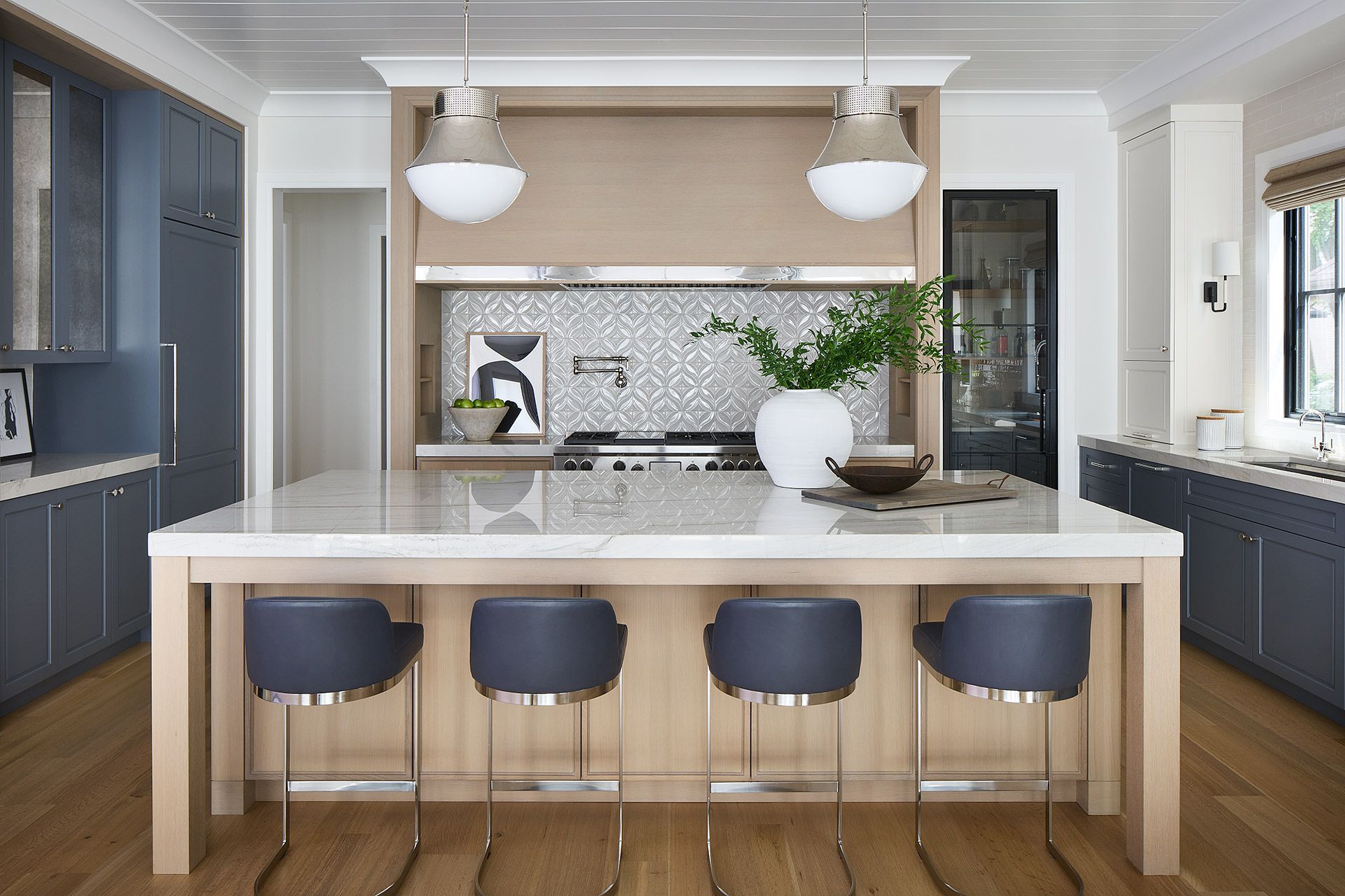 Modern kitchen with large island, four stools, white counters, pendant lights, and blue cabinets