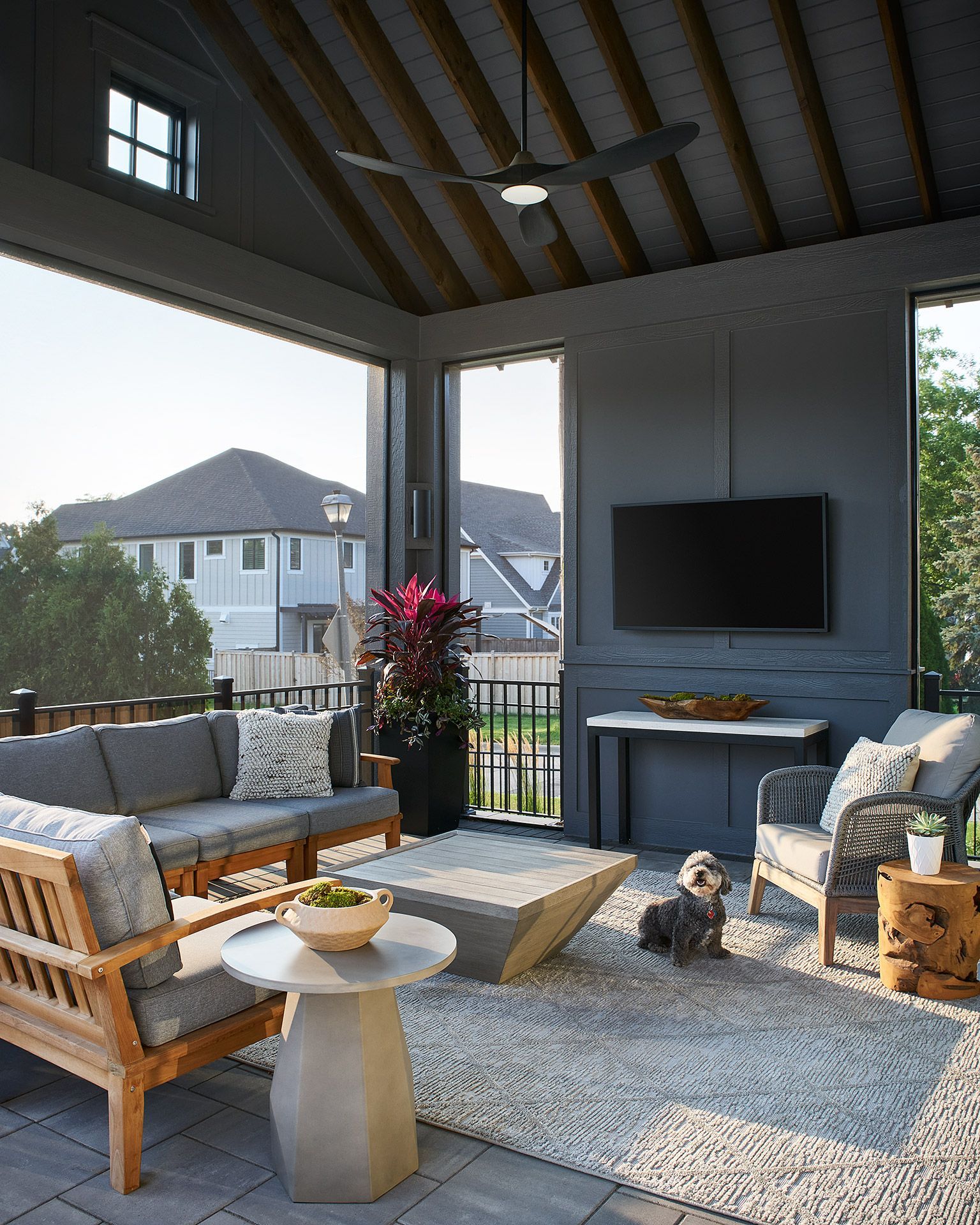 Covered patio with wicker seating, TV, fire pit table, and a small dog on a rug.