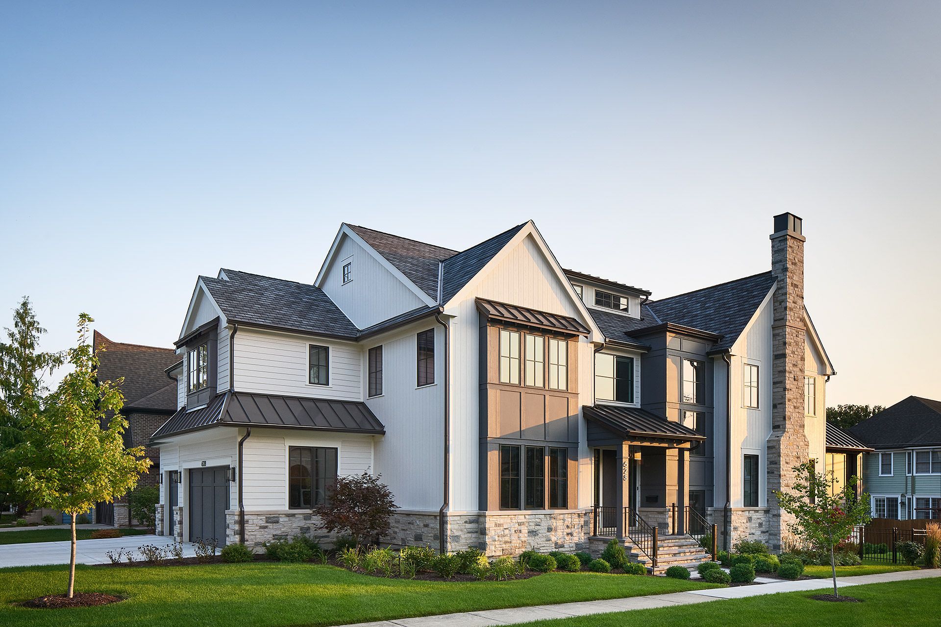 Large modern white house with dark roof, stone accents, and a manicured lawn at sunset