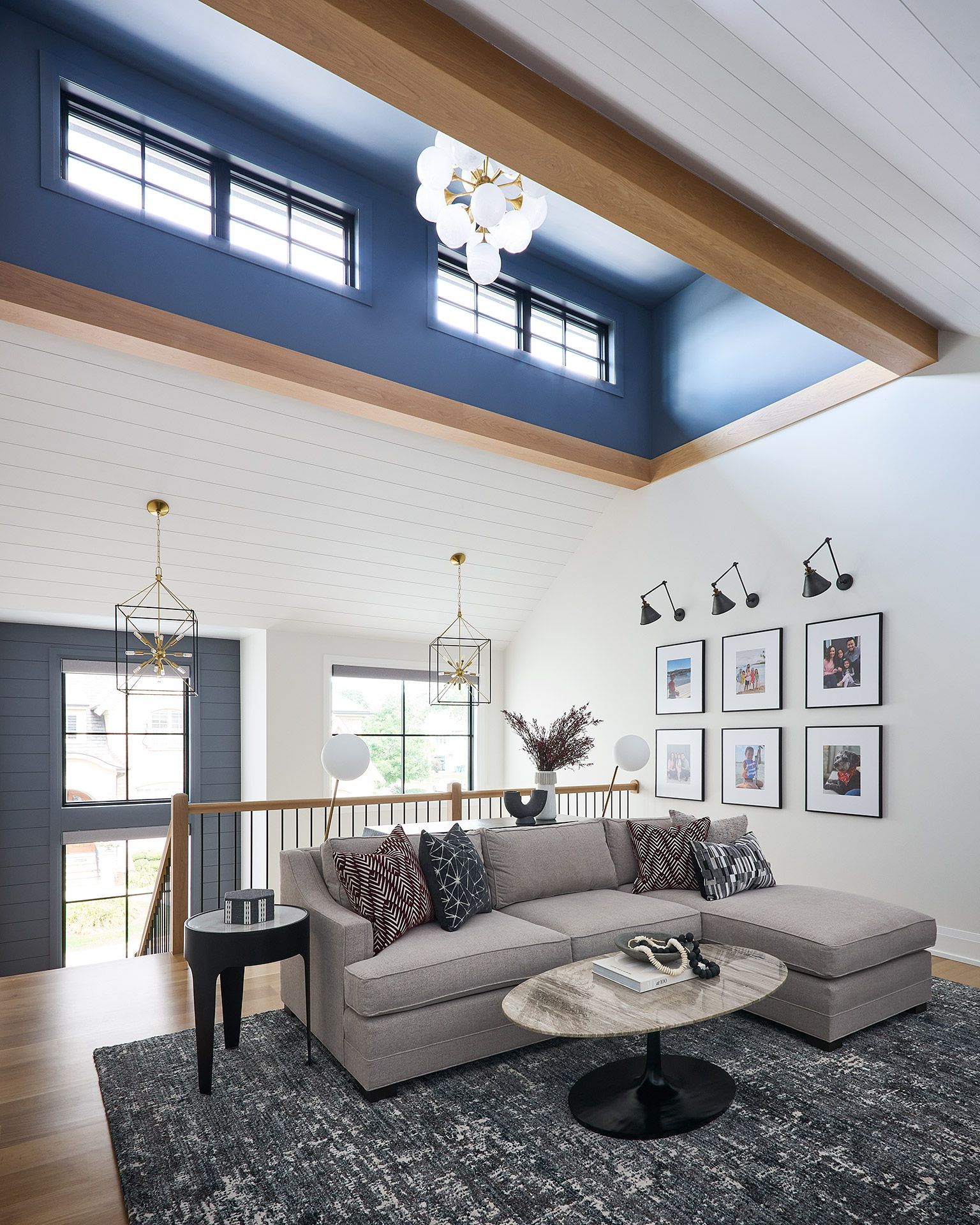 Modern living room with tall windows, blue accent wall, gray sectional, and patterned rug