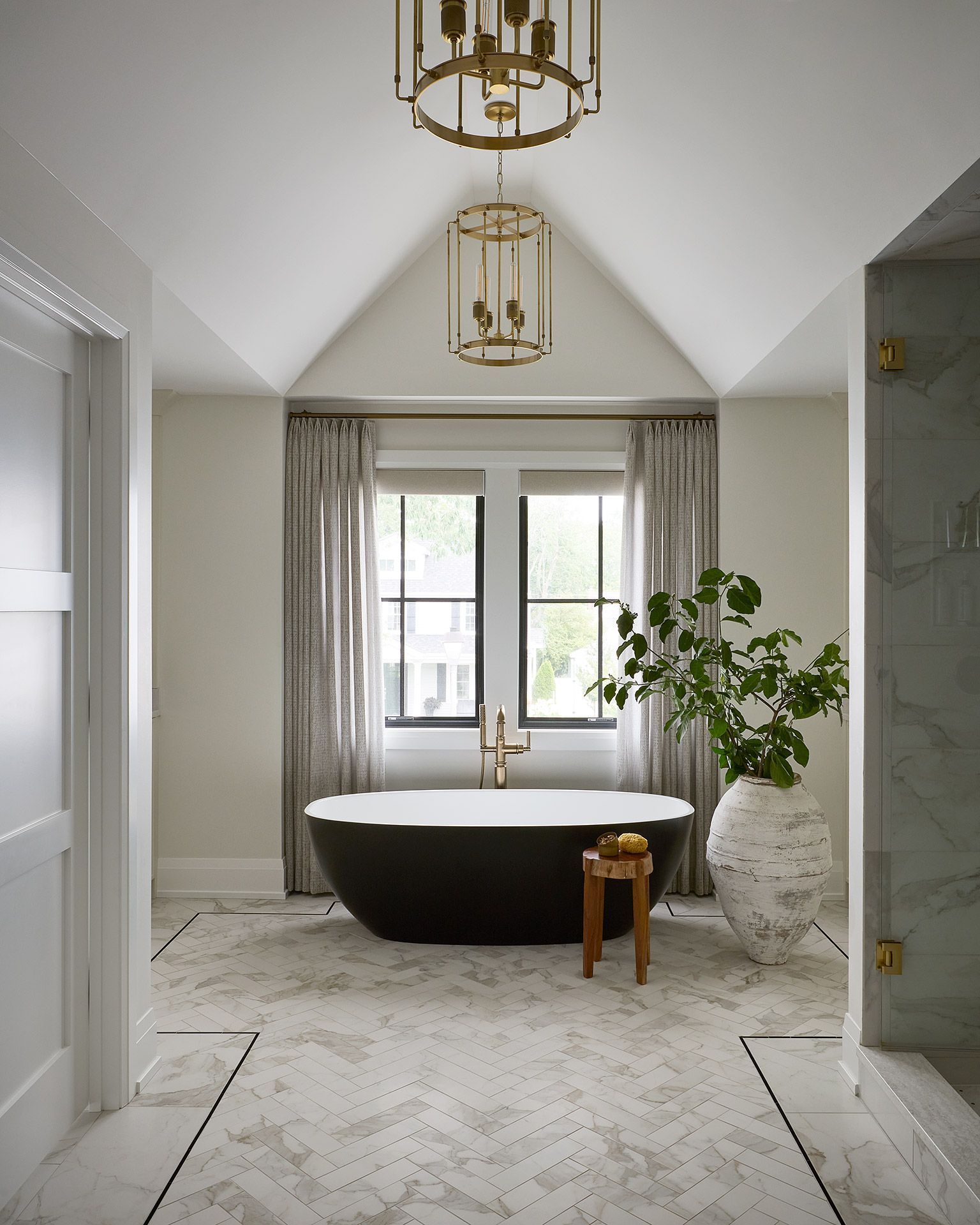 Elegant bathroom with freestanding tub, marble floor, gold pendant lights, and a potted plant by the window