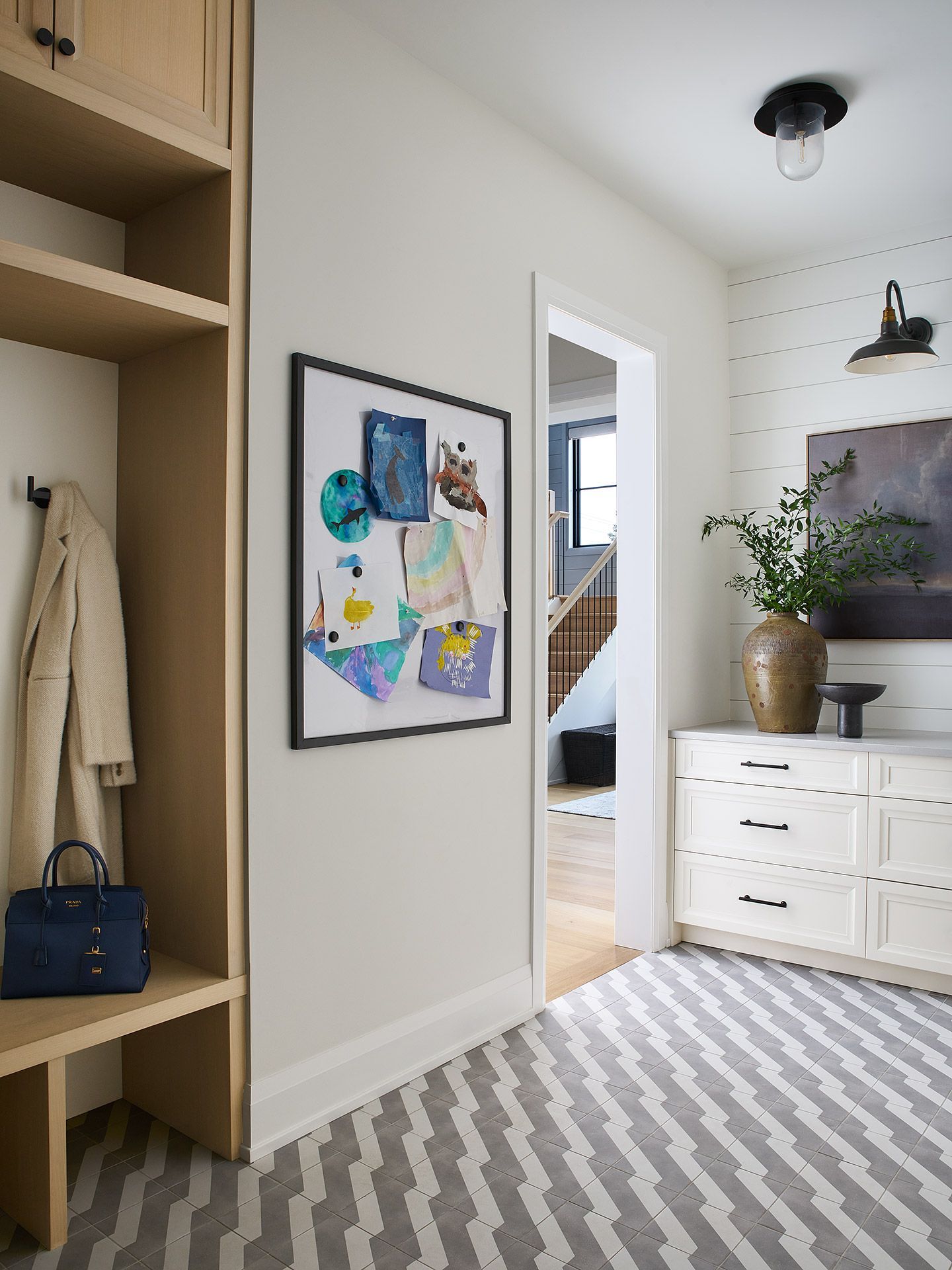 Bright hallway with striped rug, built-in shelves, framed art, and a white dresser with a plant and lamp.