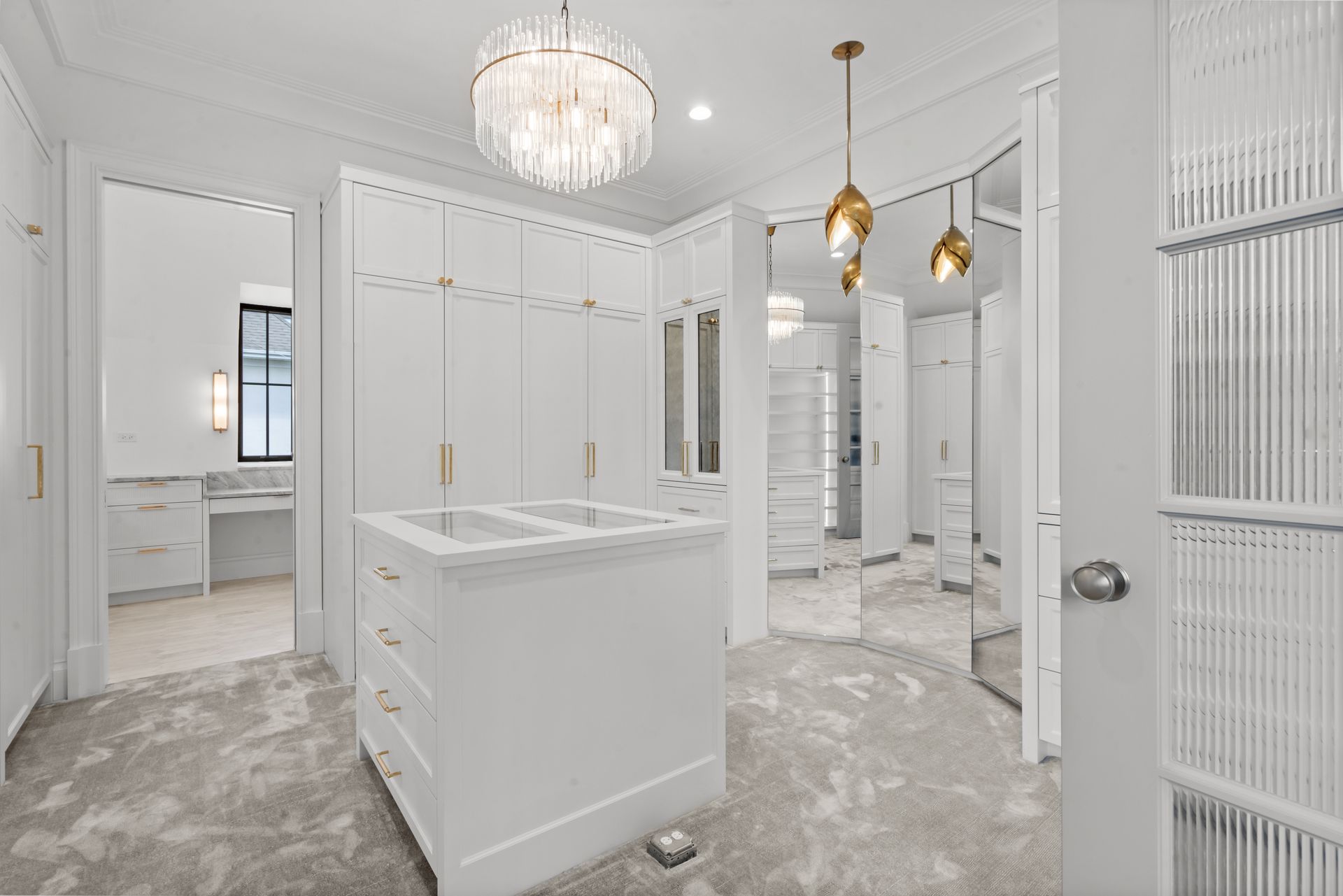 Bright white walk-in closet with island, built-in cabinets, mirrored doors, and chandelier lighting