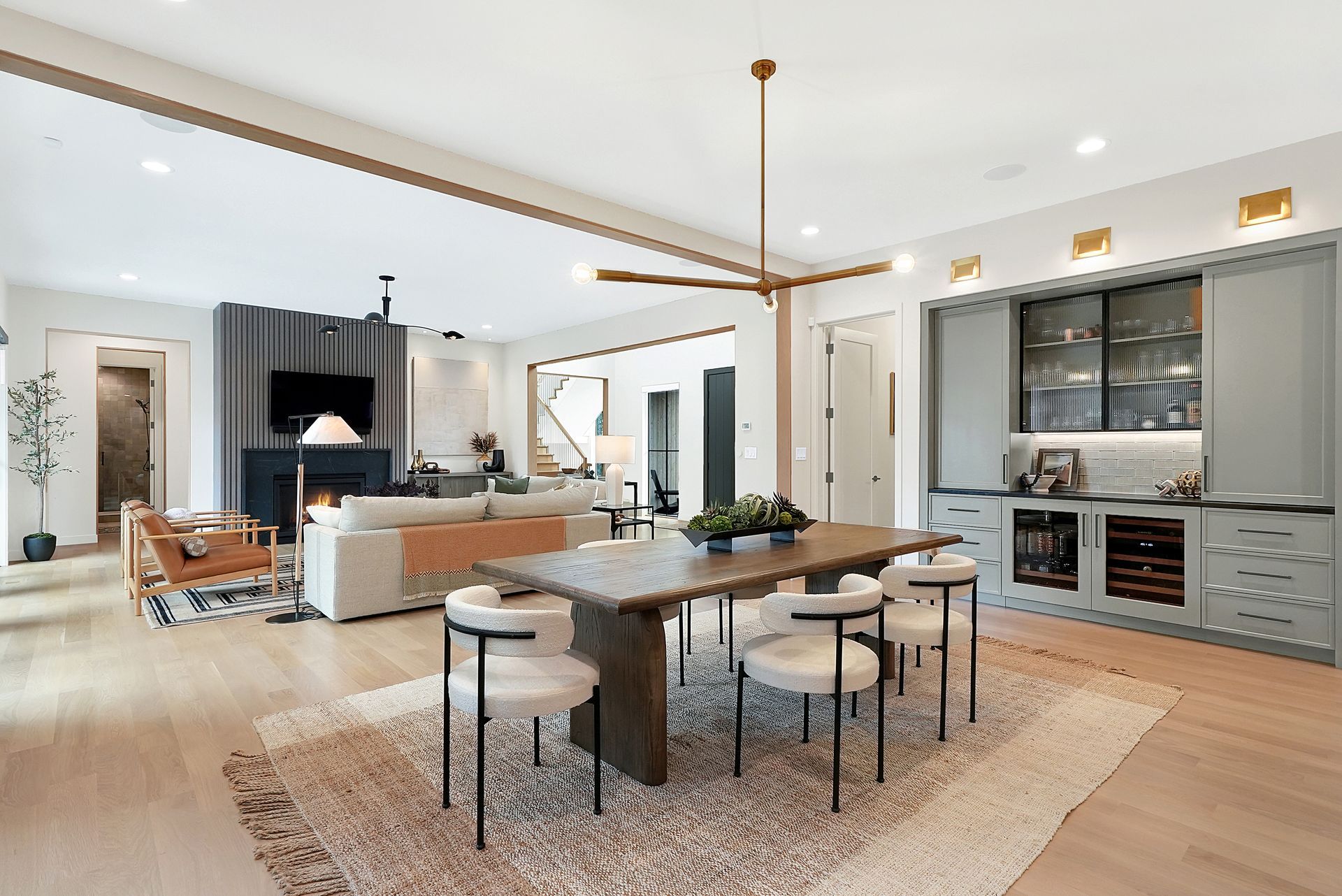 Modern open-concept kitchen and living room with light wood floors, gray cabinets, and a central dining table.