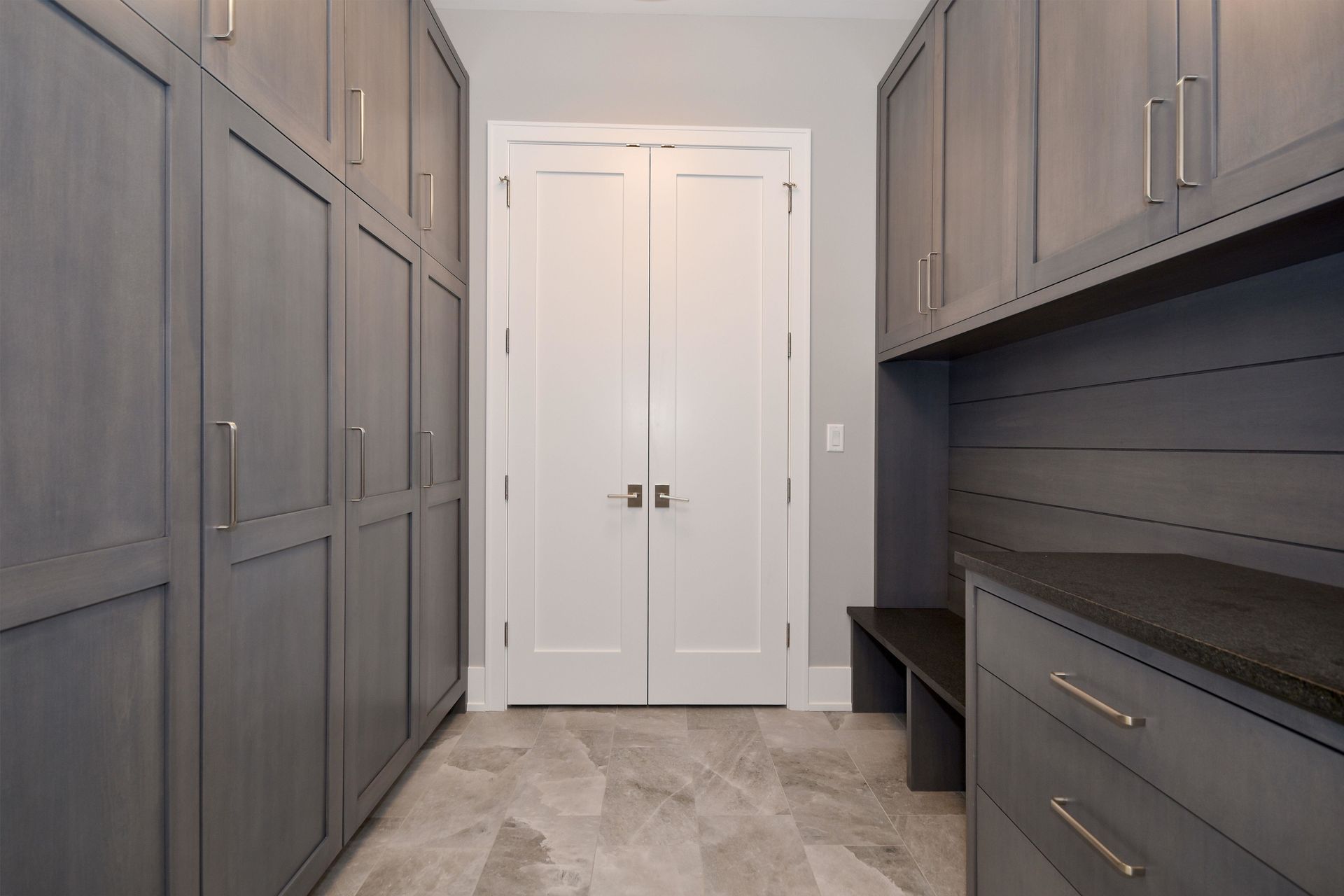 Built-in closet and entryway with gray cabinets, white double doors, and light tile floor