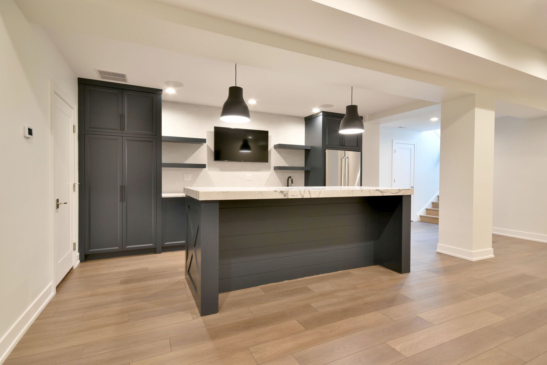 Modern open-plan kitchen with dark cabinets, white island, pendant lights, and wood floors
