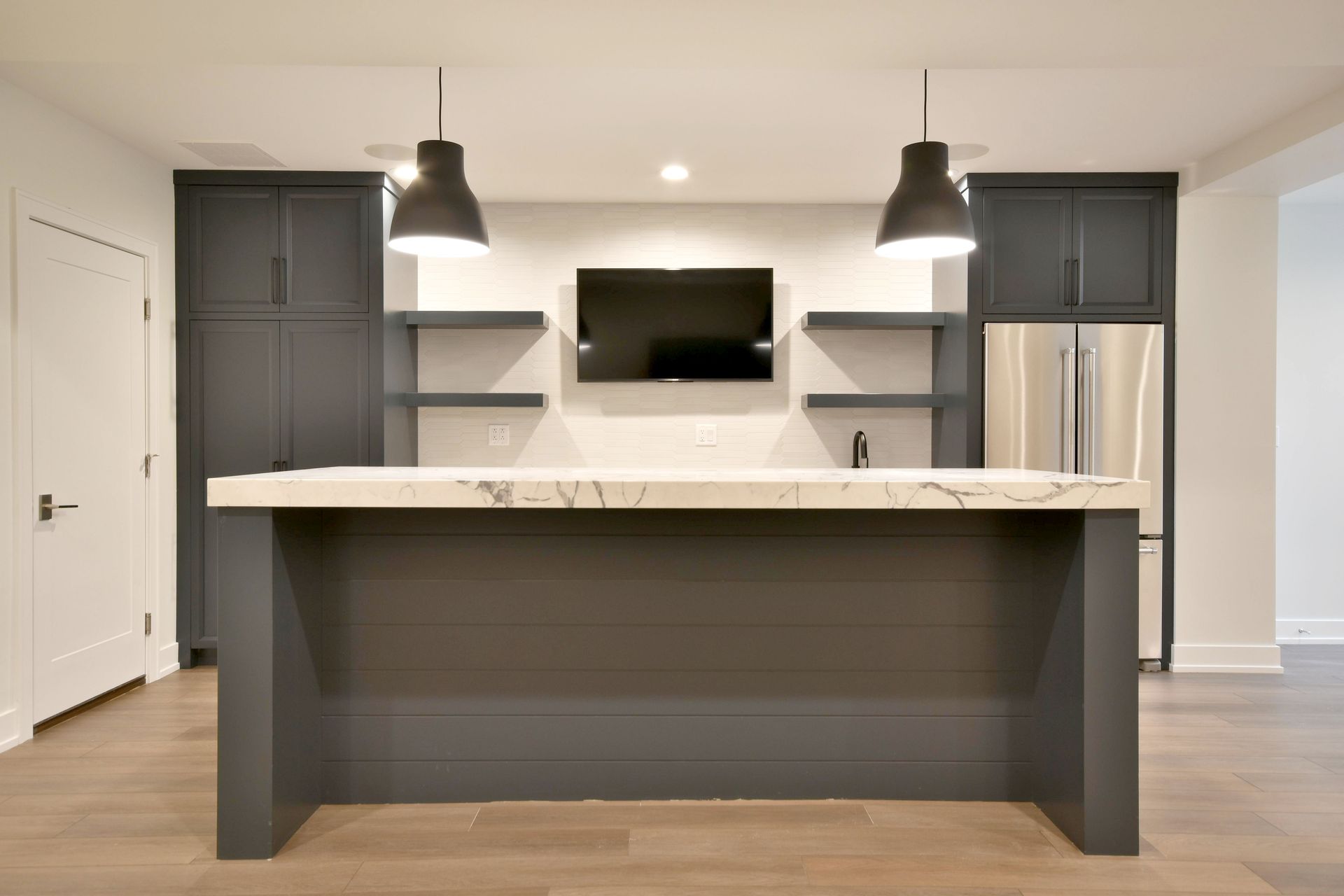 Modern kitchen with large island, pendant lights, gray cabinetry, and wall-mounted TV