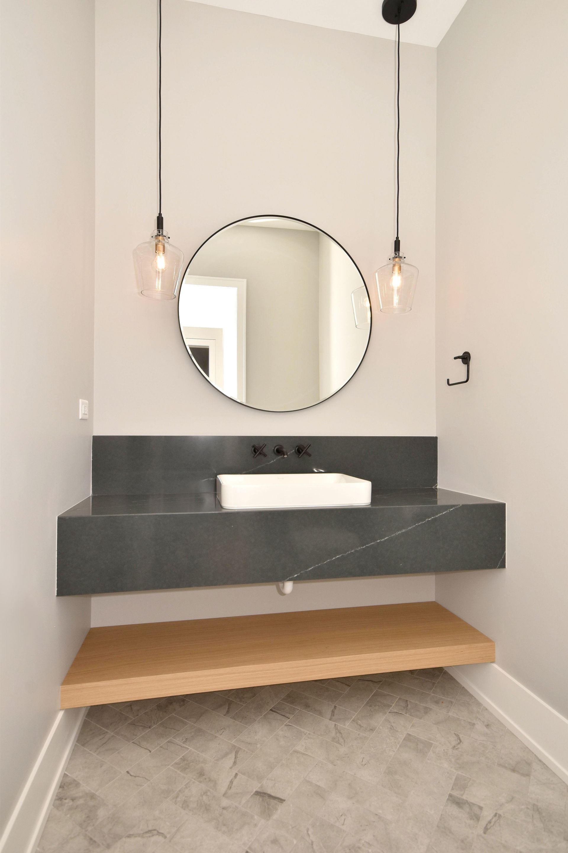 Modern bathroom vanity with round mirror, black sink, and hanging pendant lights
