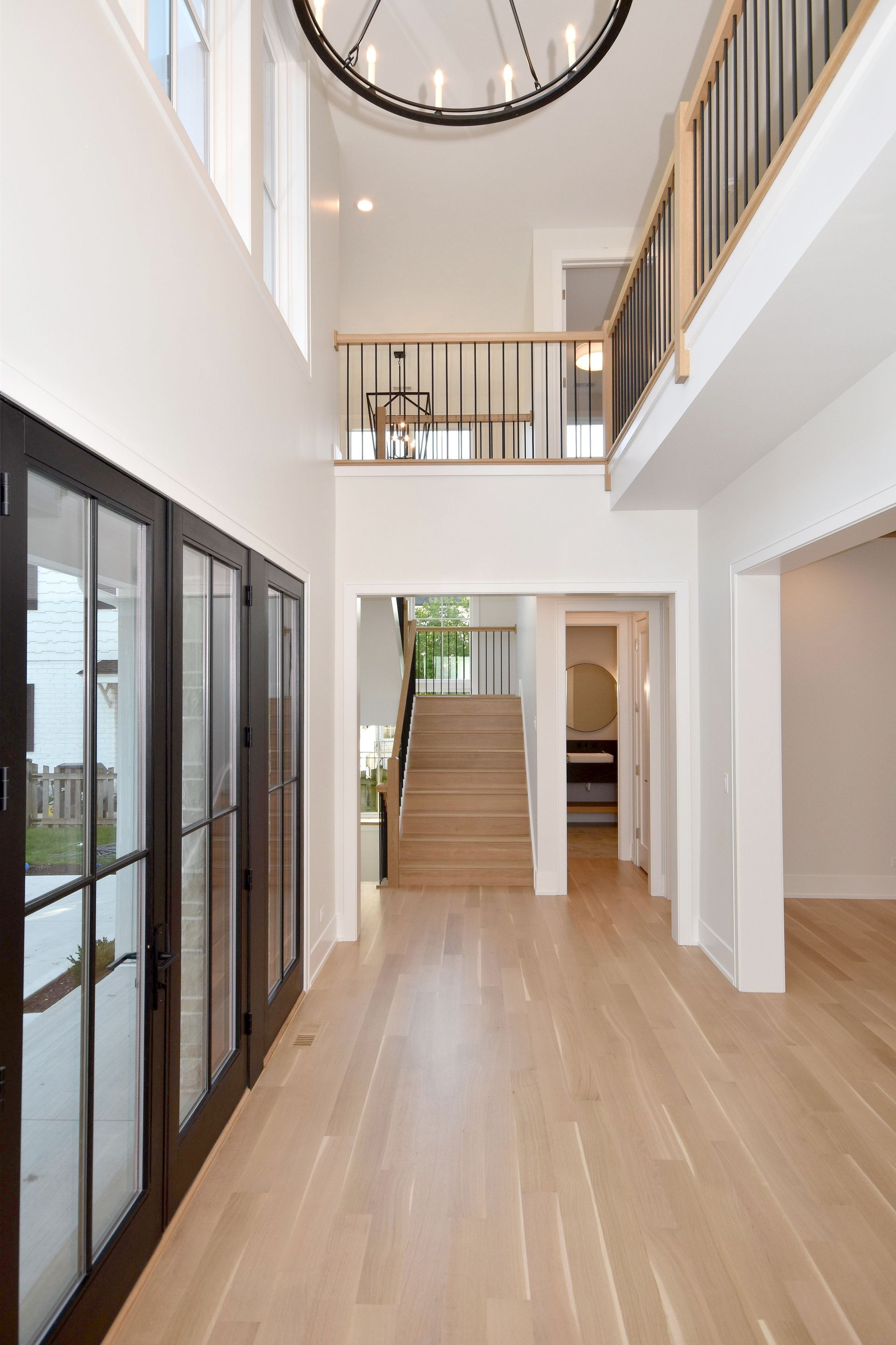 Bright modern foyer with wood floors, staircase, glass doors, and upper balcony railing