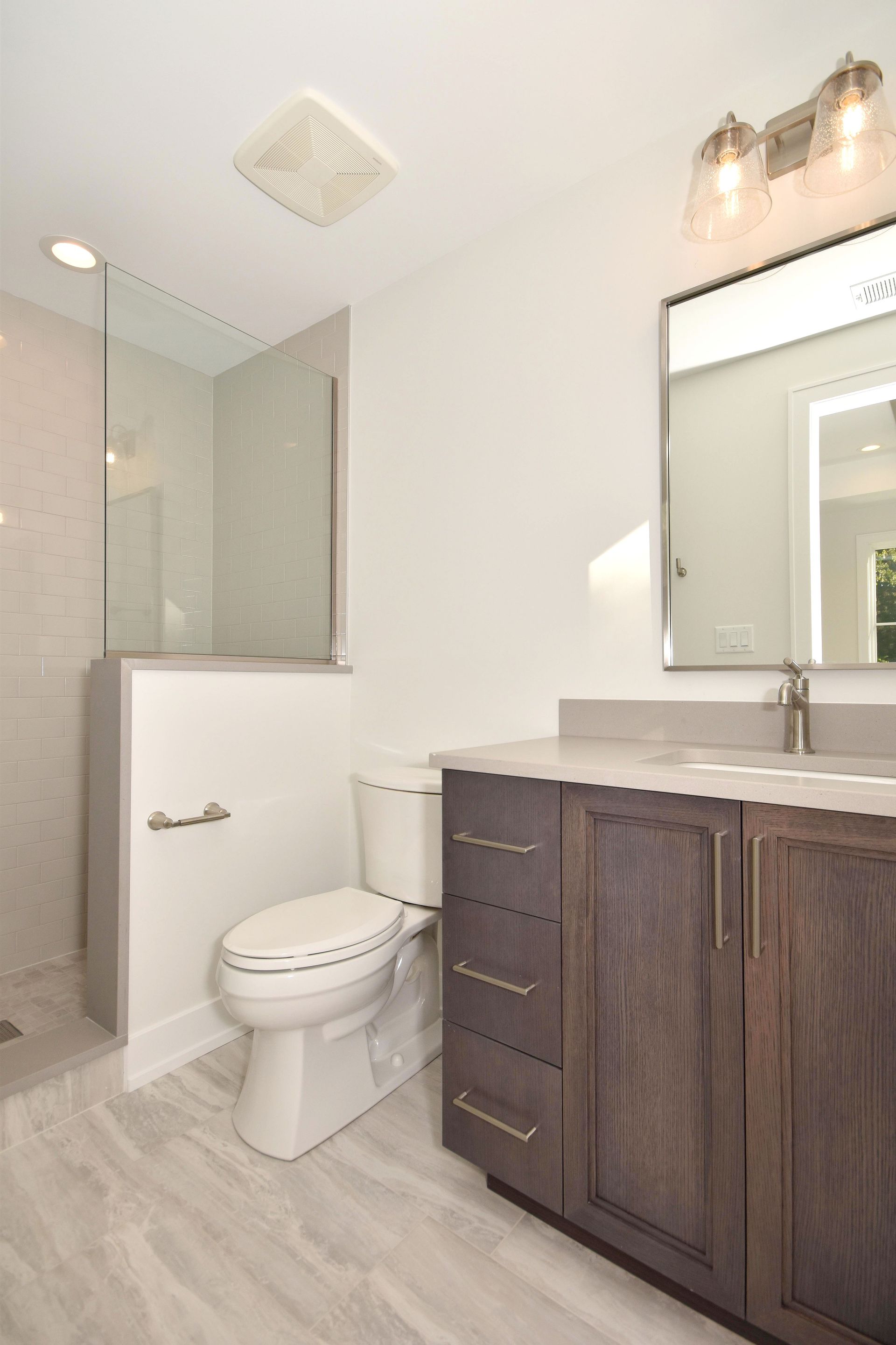 Modern bathroom with glass shower, toilet, and dark wood vanity with mirror on white walls.