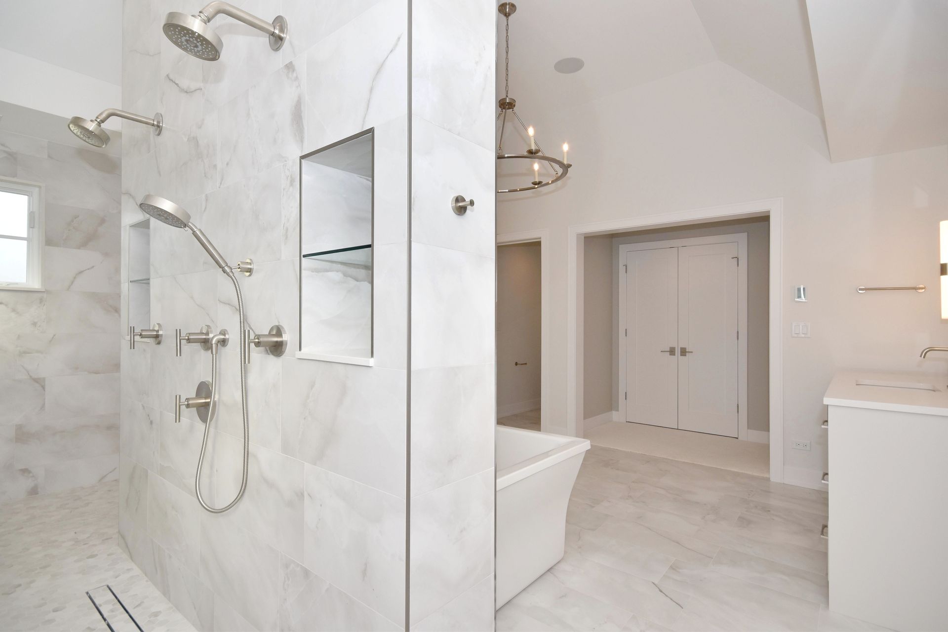 Bright modern bathroom with white marble shower, glass door, and double vanity.
