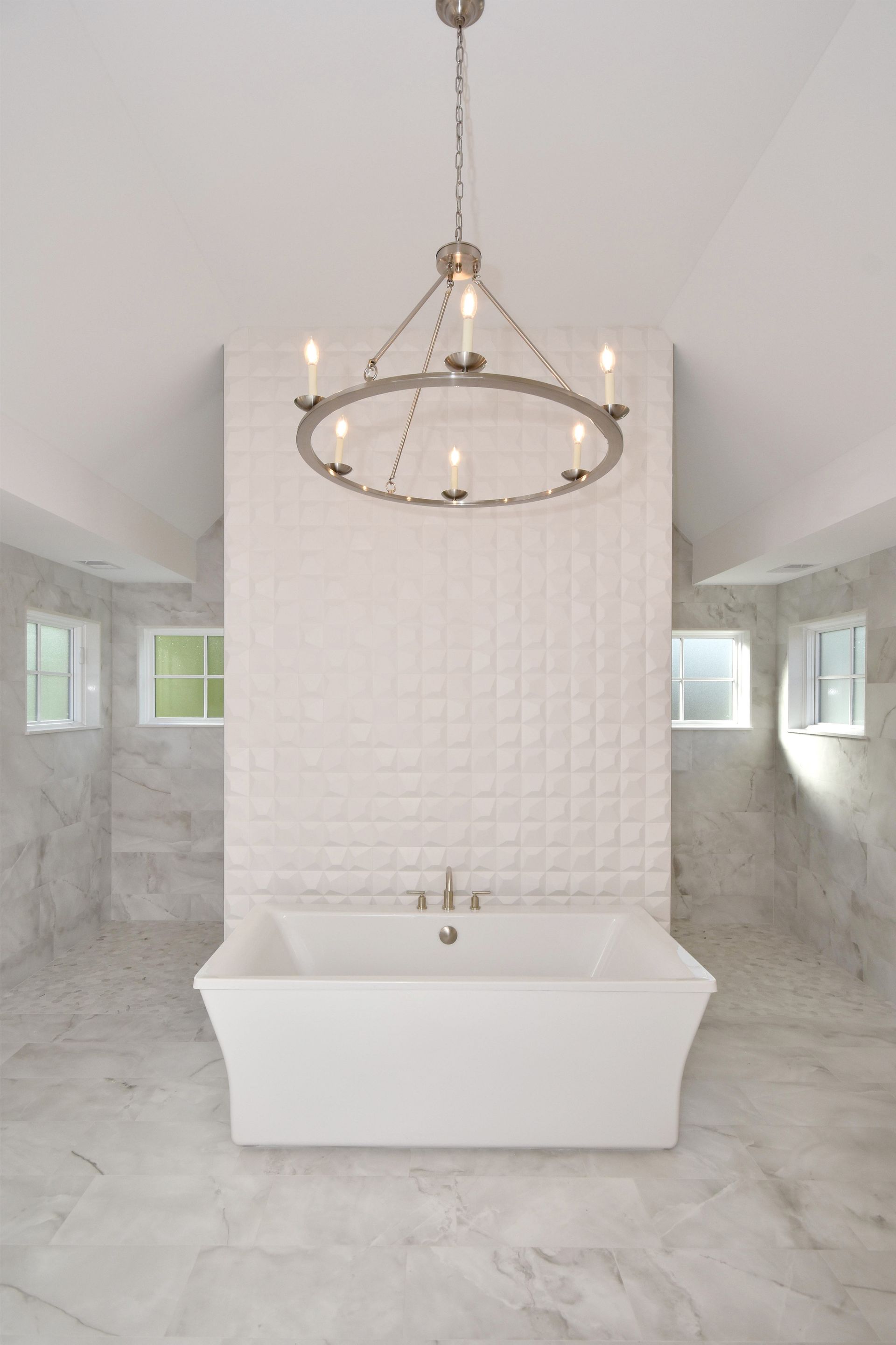 Modern white bathroom with freestanding tub, chandelier, and tiled walls in a bright, symmetrical space