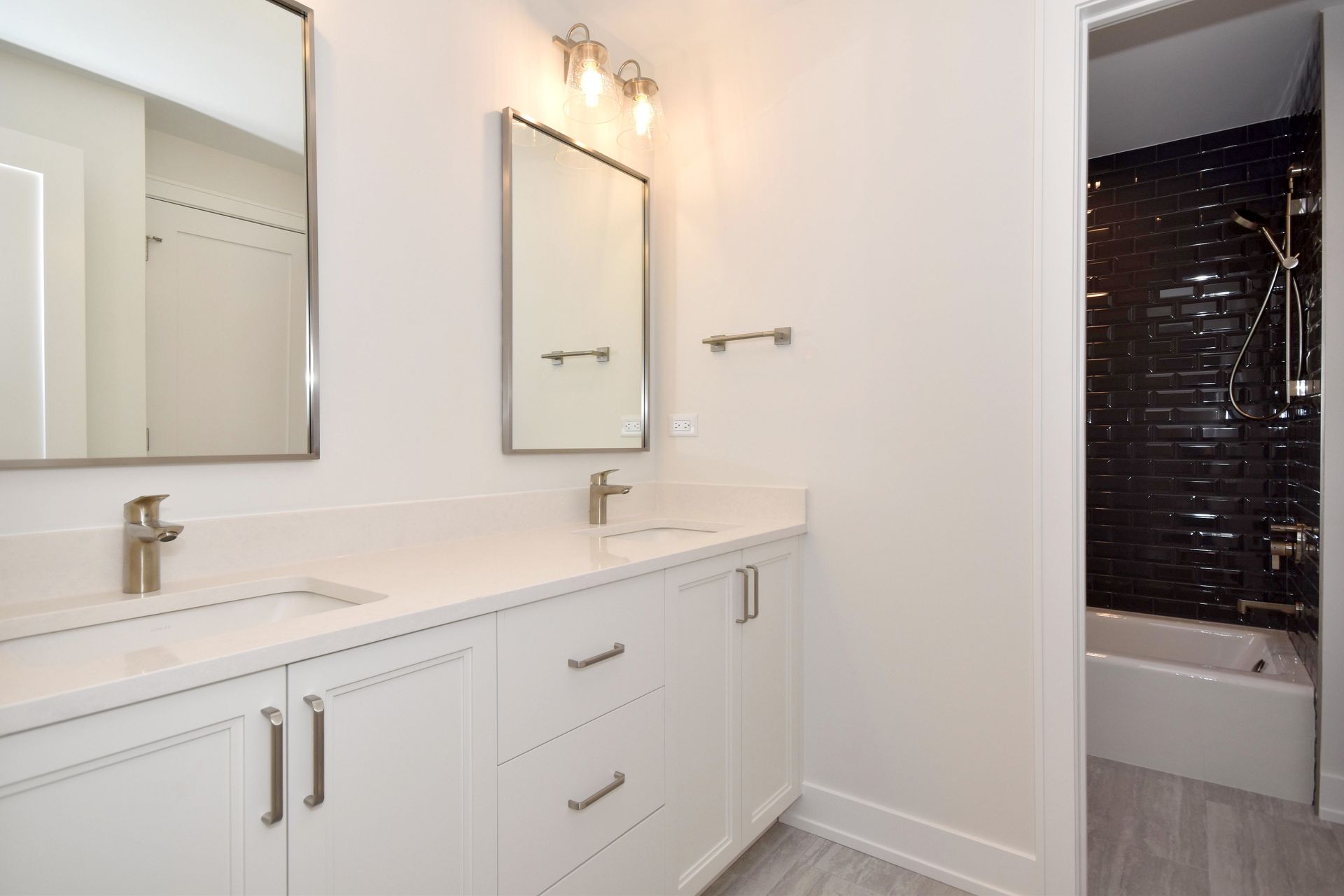 Bright bathroom vanity with white cabinets, mirror, lights, and a glimpse of a tiled shower.