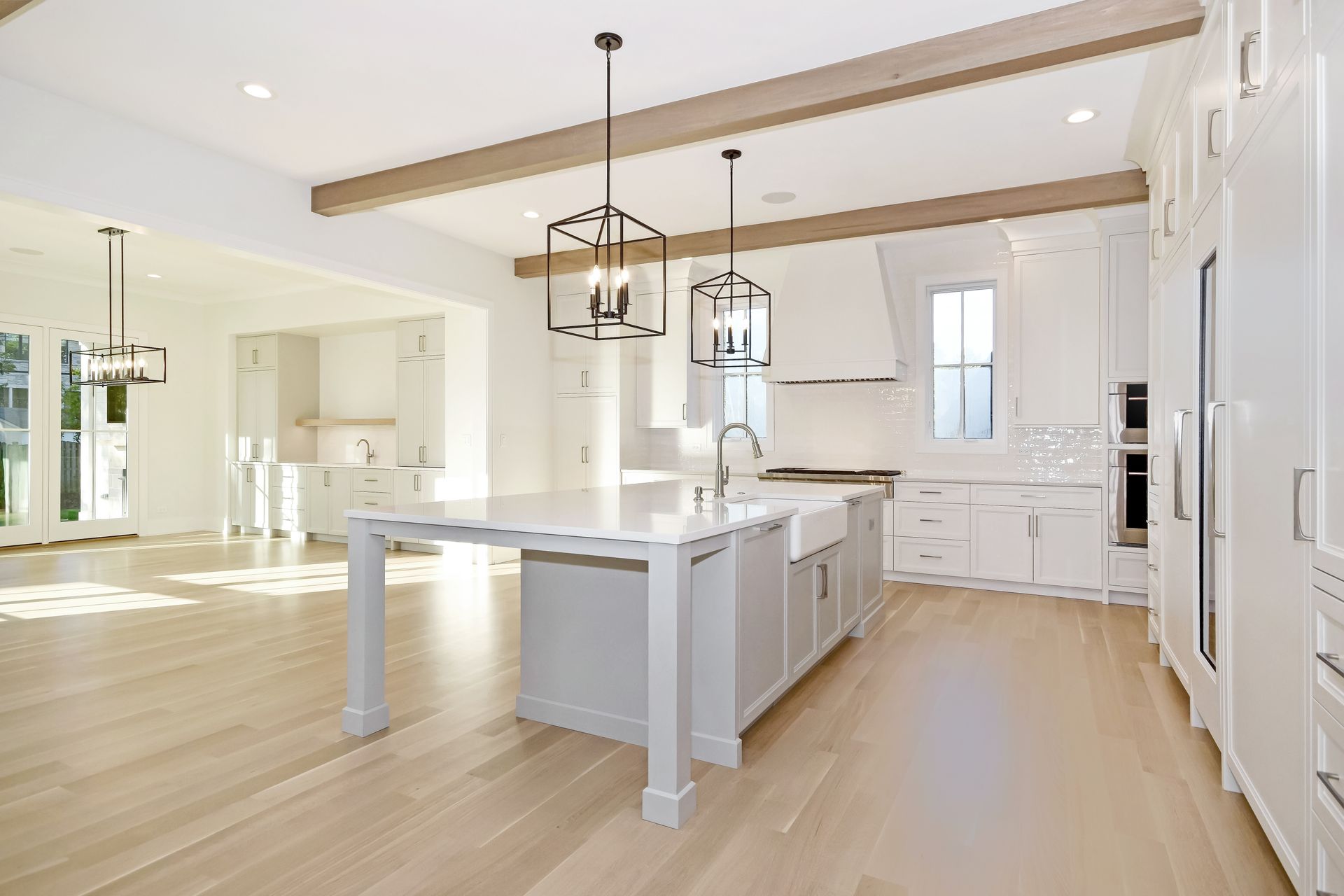 Bright modern kitchen with white cabinets, island, and light wood floors under exposed beams