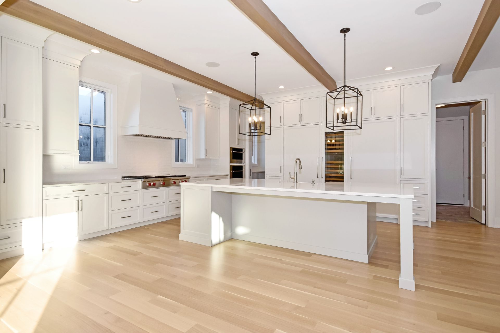 Bright modern white kitchen with island, wood floors, pendant lights, and exposed ceiling beams