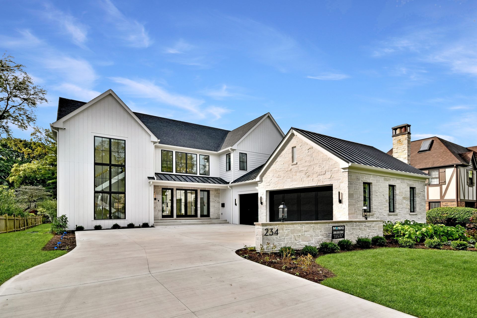 Modern white two-story house with black garage doors, large windows, and a landscaped driveway