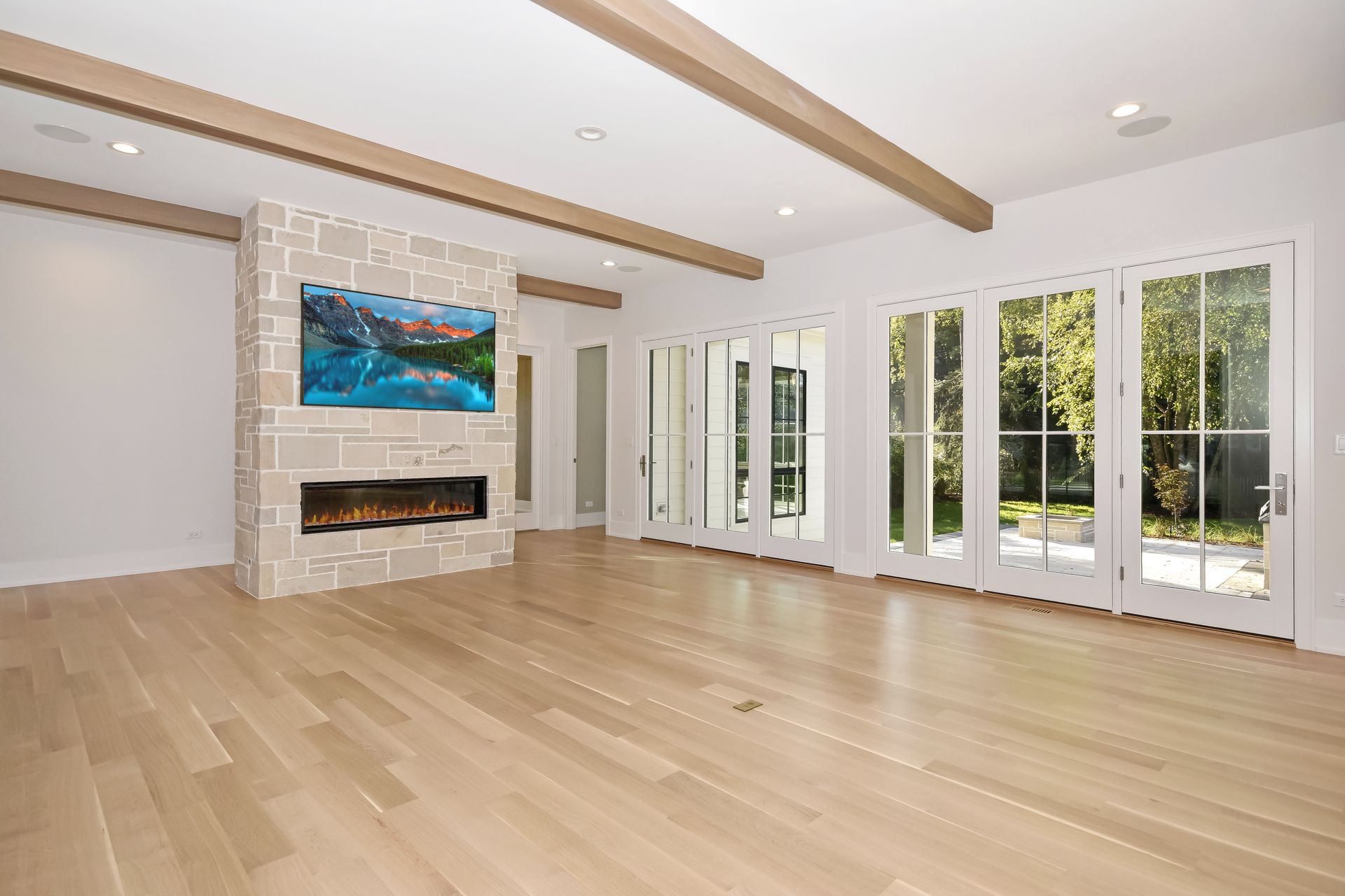 Bright empty living room with wood floors, stone fireplace, skylights, and glass doors to a green patio