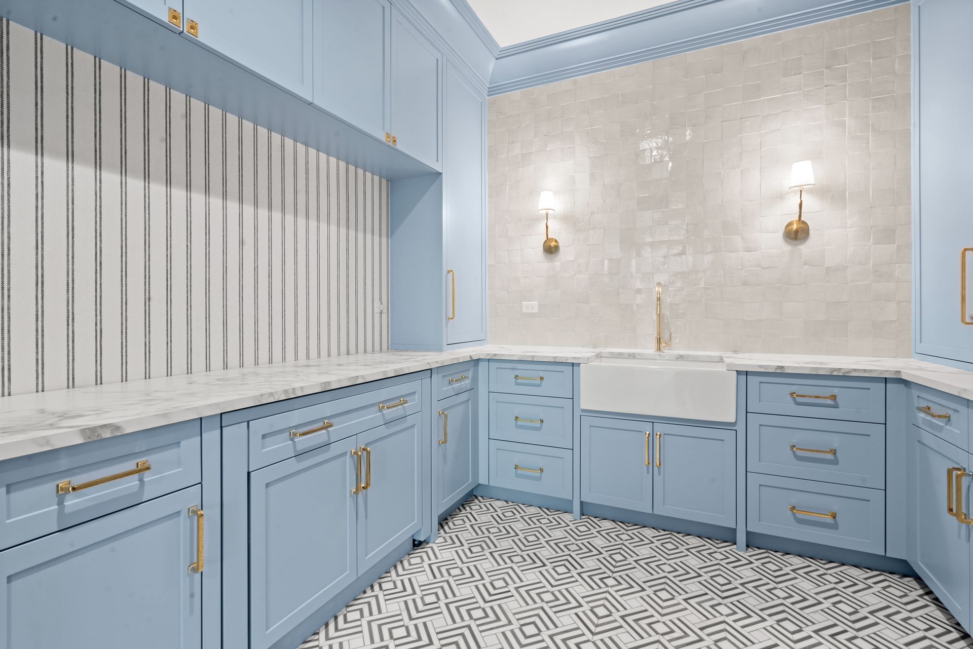 Blue vanity bathroom with patterned black-and-white floor and marble wall, featuring double sinks and brass sconces