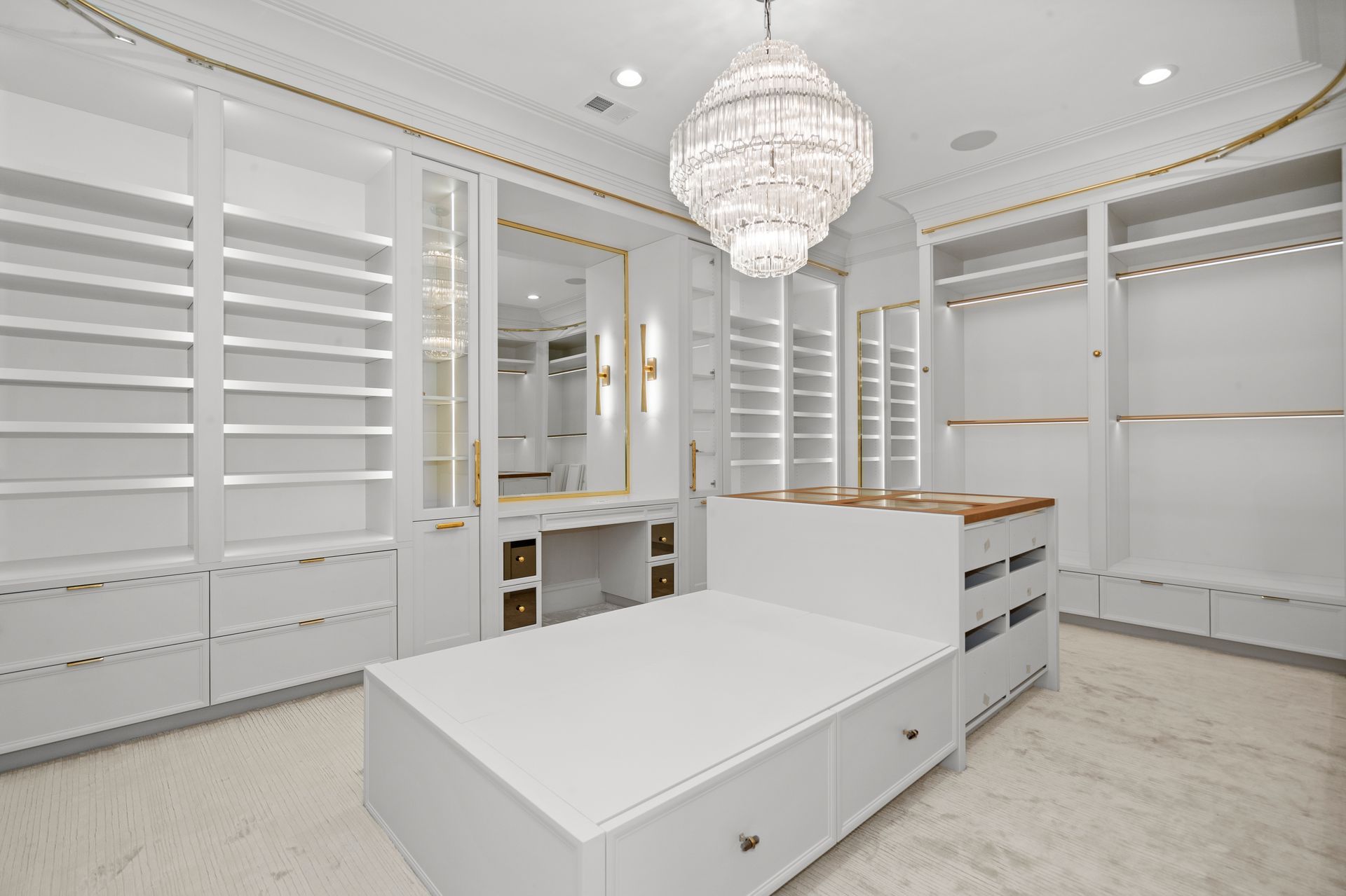 Bright white walk-in closet with chandeliers, built-in shelves, mirrors, and a central island.