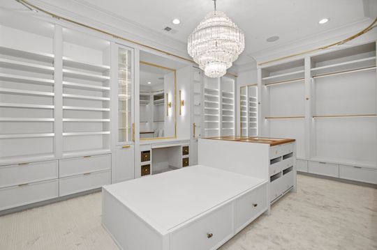 Bright white walk-in closet with built-in shelving, drawers, mirrors, and a crystal chandelier
