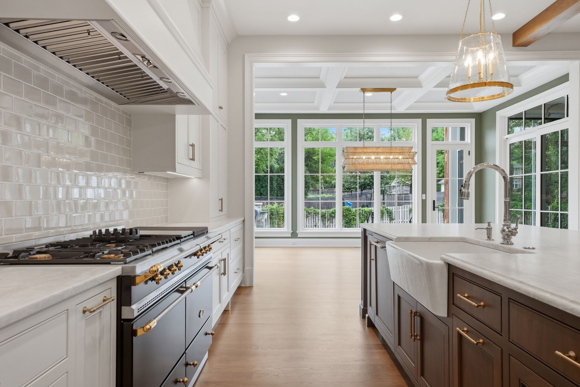 Bright modern kitchen with white cabinets, dark island, marble counters, and large windows overlooking greenery
