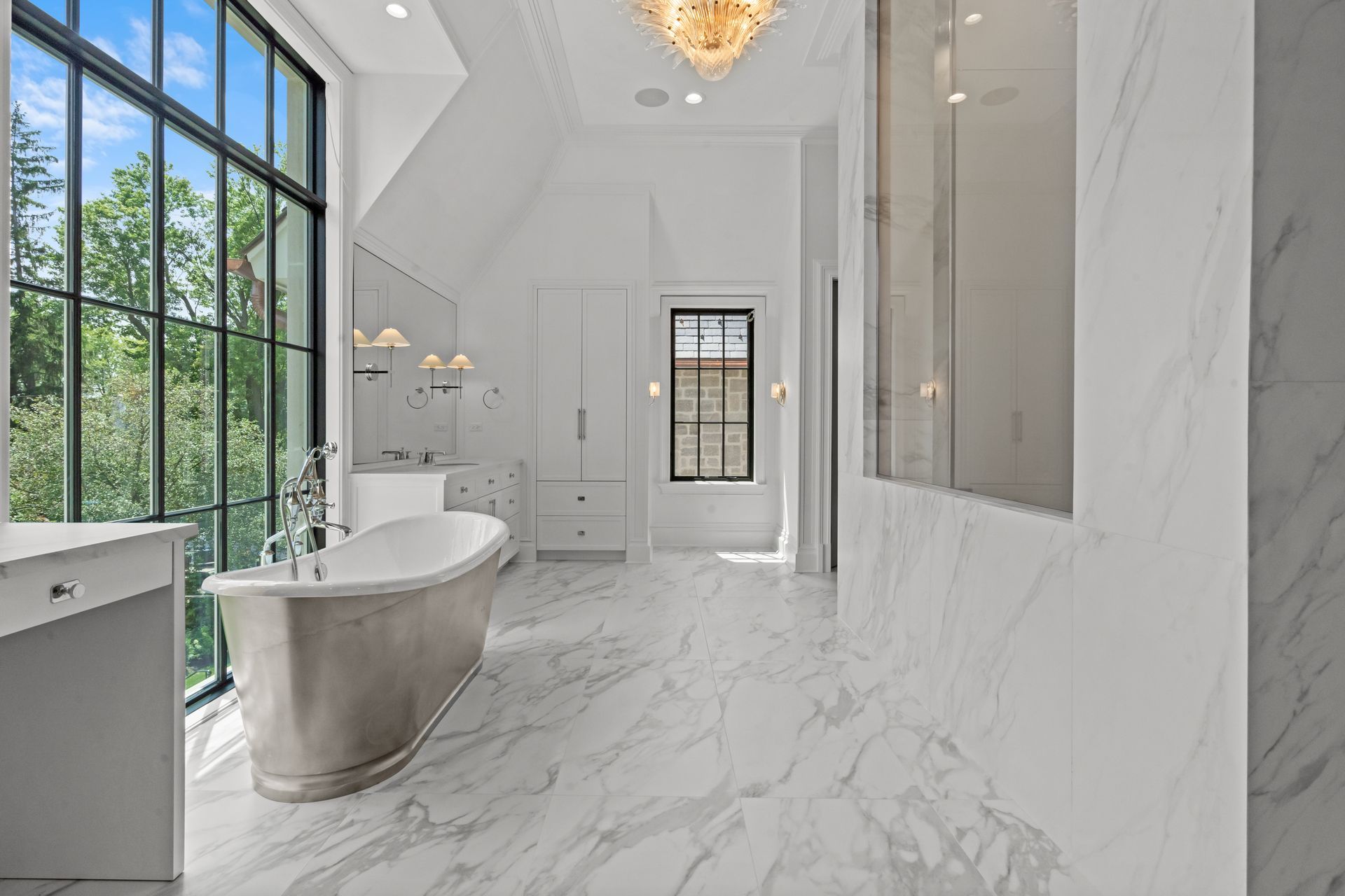 Luxury white marble bathroom with freestanding tub, large window, and chandelier