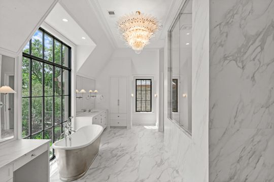 Bright marble bathroom with freestanding tub, chandelier, and large black-framed windows