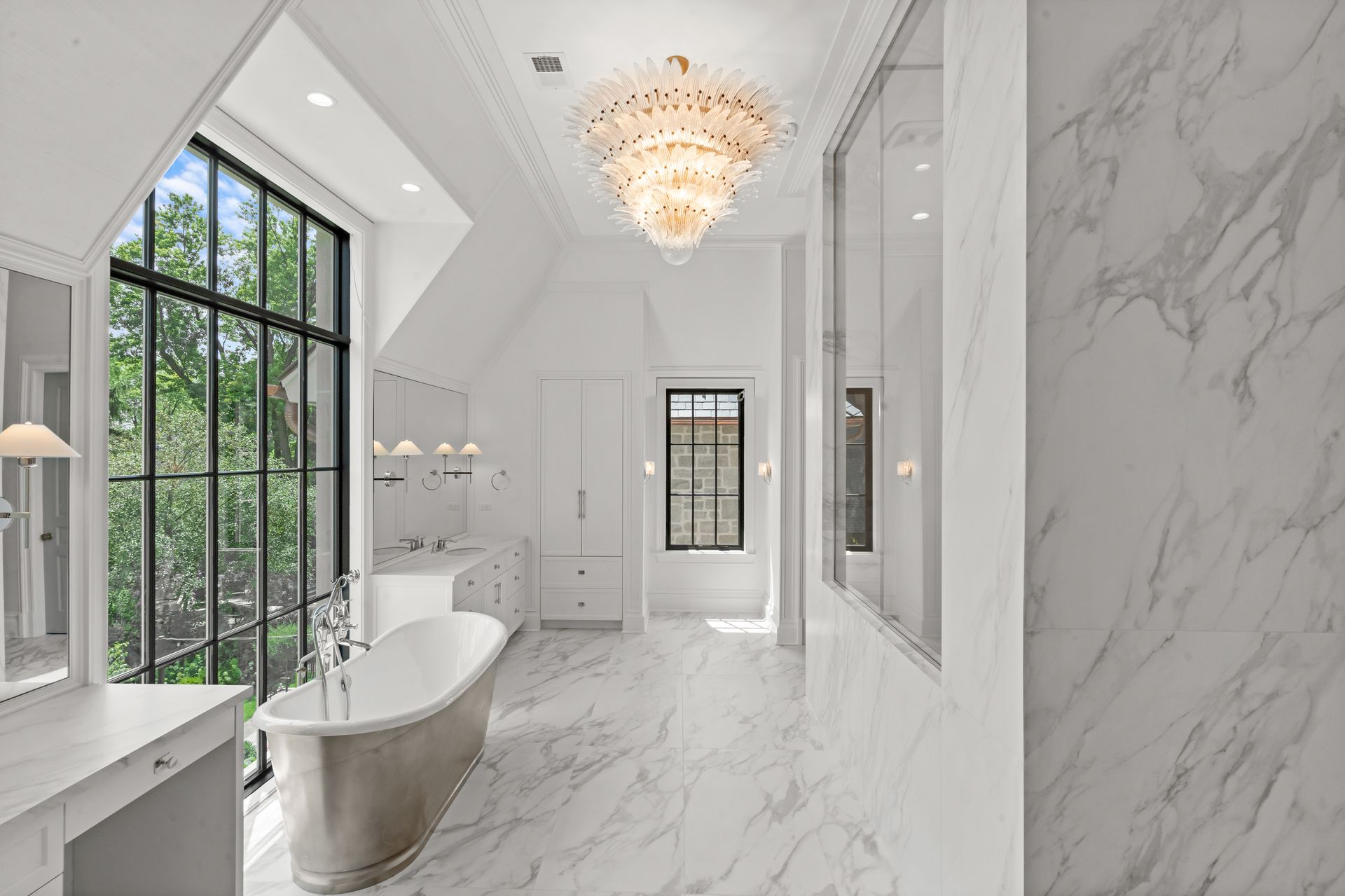 Elegant white marble bathroom with a freestanding tub, chandelier, and large black-framed windows