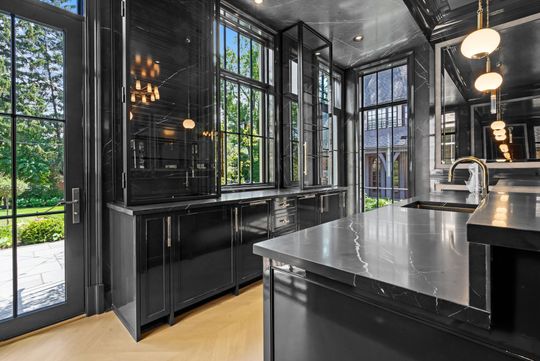Modern black kitchen with glossy cabinets, marble island, and floor-to-ceiling windows overlooking greenery