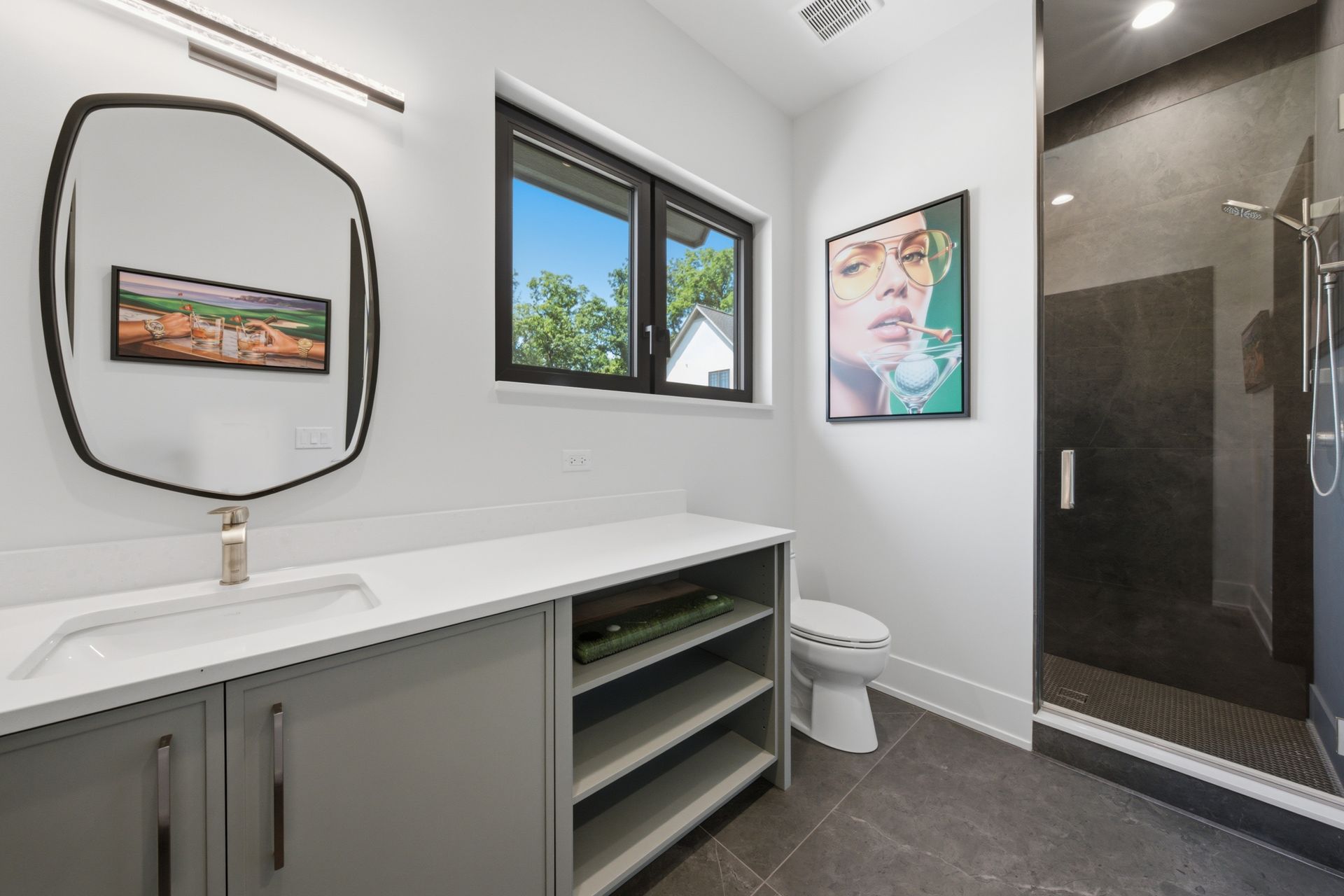 Modern bathroom with vanity, mirror, window, artwork, toilet, and glass shower enclosure