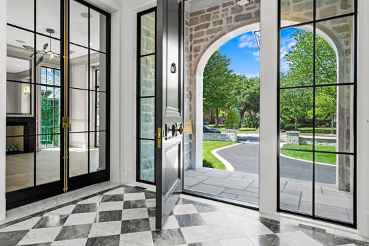 Modern entryway with black-and-white tiled floor, glass doors, and an arched view to a green garden outside