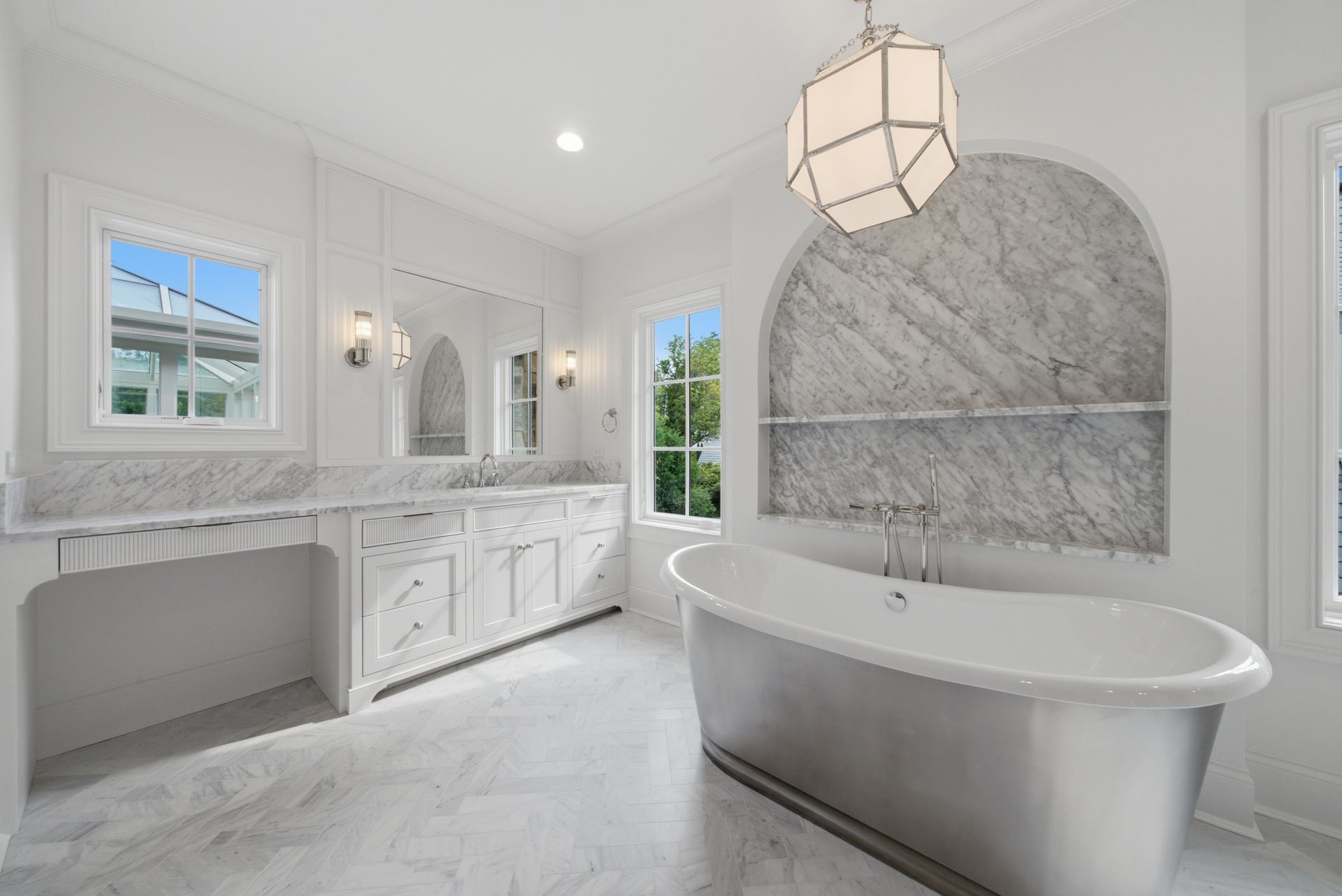Bright white marble bathroom with double vanity, arched shower niche, and freestanding tub