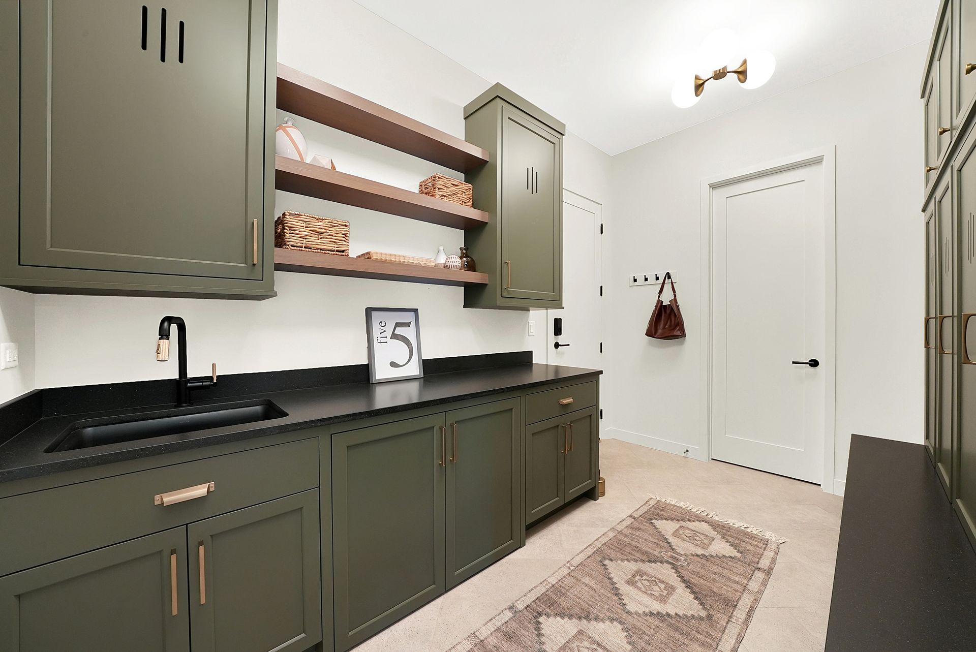 Green kitchen with black countertops, open wooden shelves, white doors, and a patterned rug.