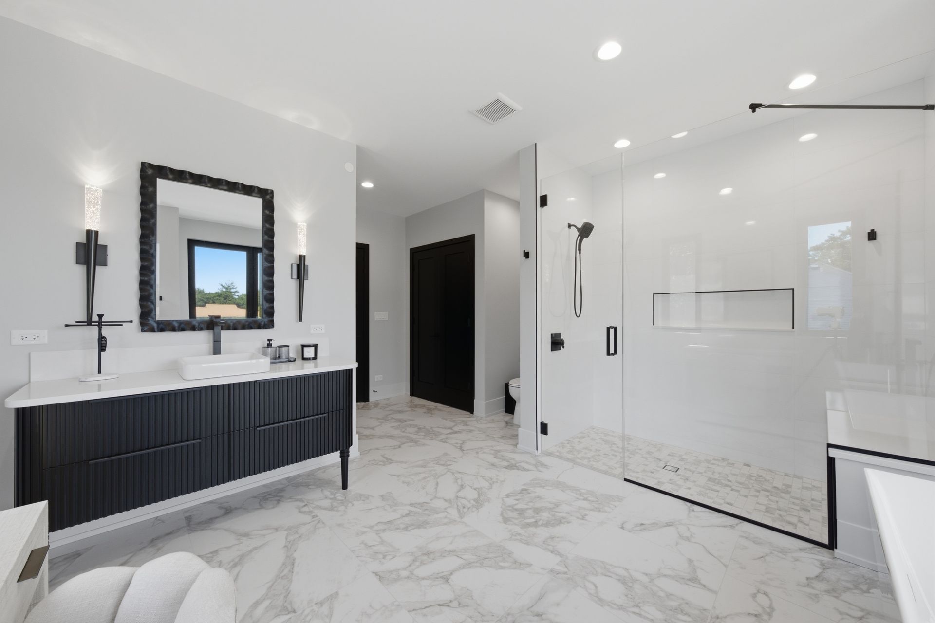 Modern white bathroom with black vanity, large mirror, walk-in glass shower, and marble-look floor tiles