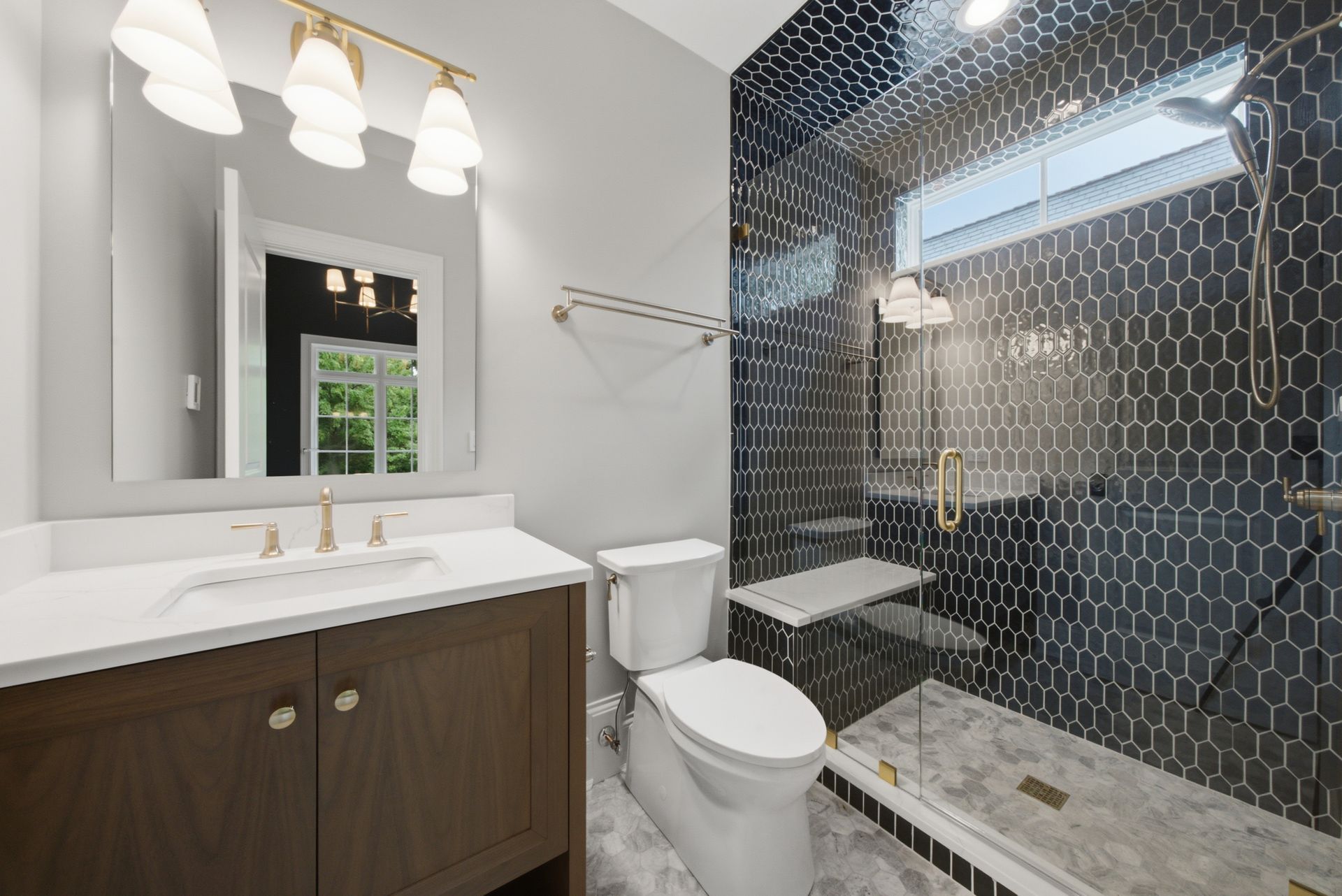 Modern bathroom with dark vanity, white sink, mirror, toilet, and black tiled shower with glass door