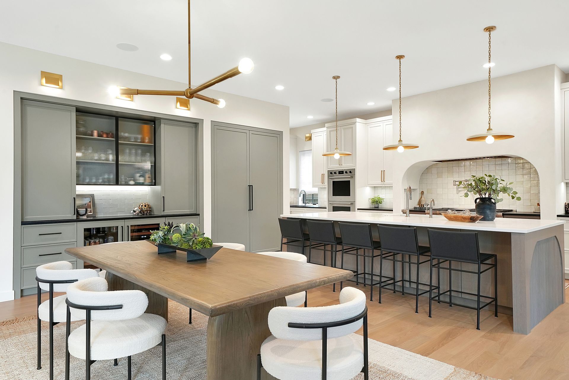 Bright modern kitchen with wood table, gray island seating, white cabinets, and brass lighting