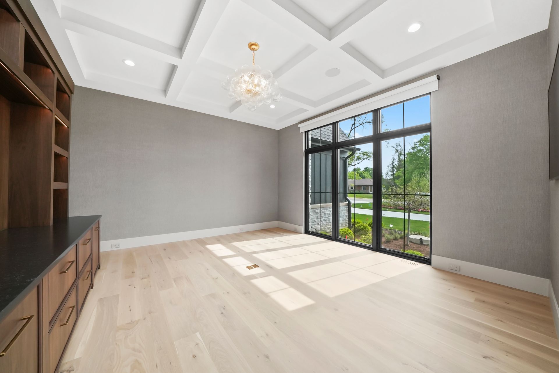 Bright empty room with light wood floors, gray walls, built-in shelving, and large glass doors to a patio.