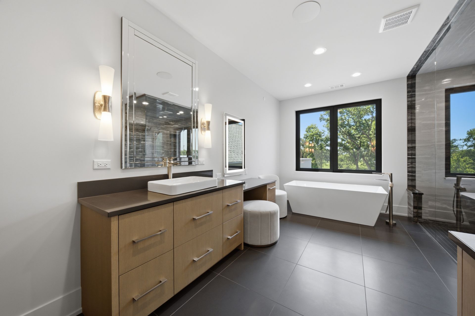 Modern bathroom with double vanity, freestanding tub, and large window overlooking greenery