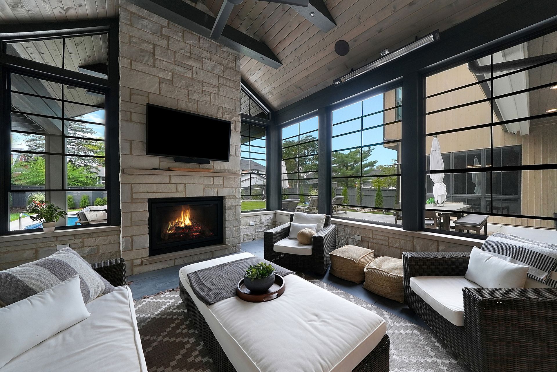 Modern living room with fireplace, large windows, neutral sofas, and a wall-mounted TV