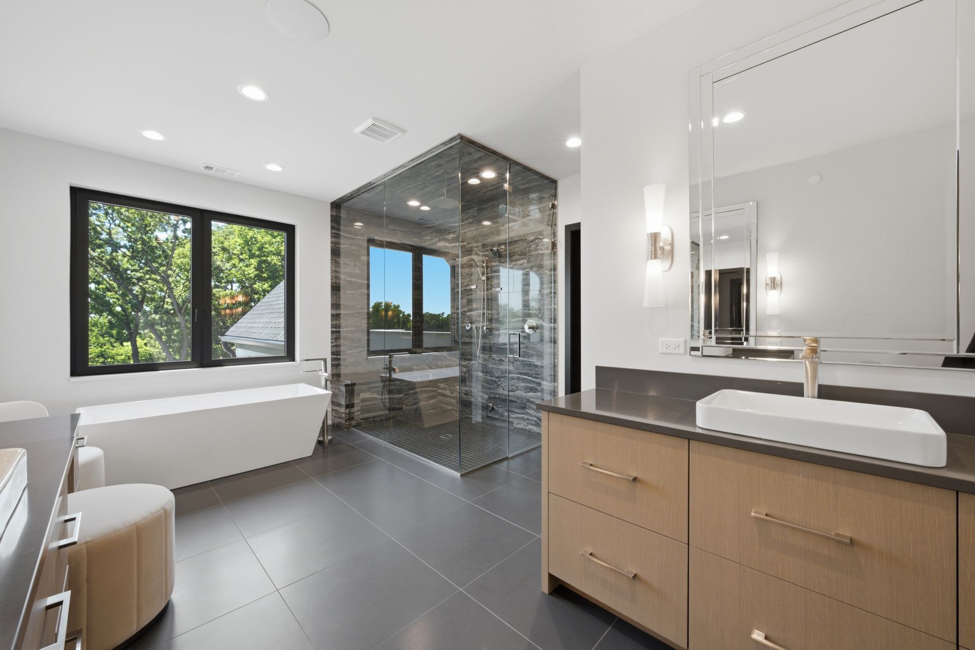 Modern bathroom with freestanding tub, glass shower, large windows, and wood vanity