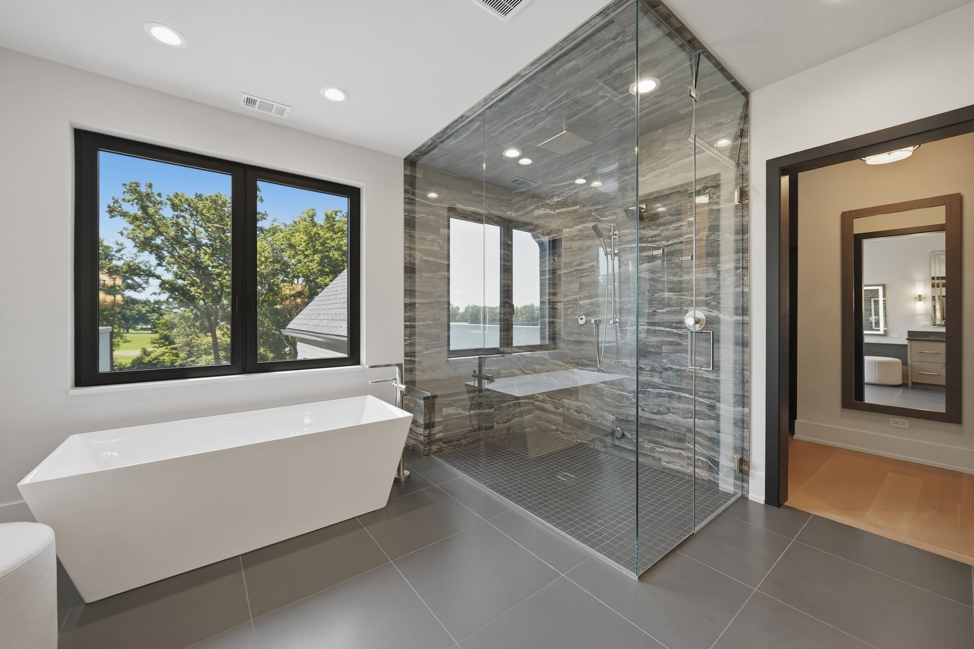 Modern bathroom with freestanding tub, glass shower, and large windows